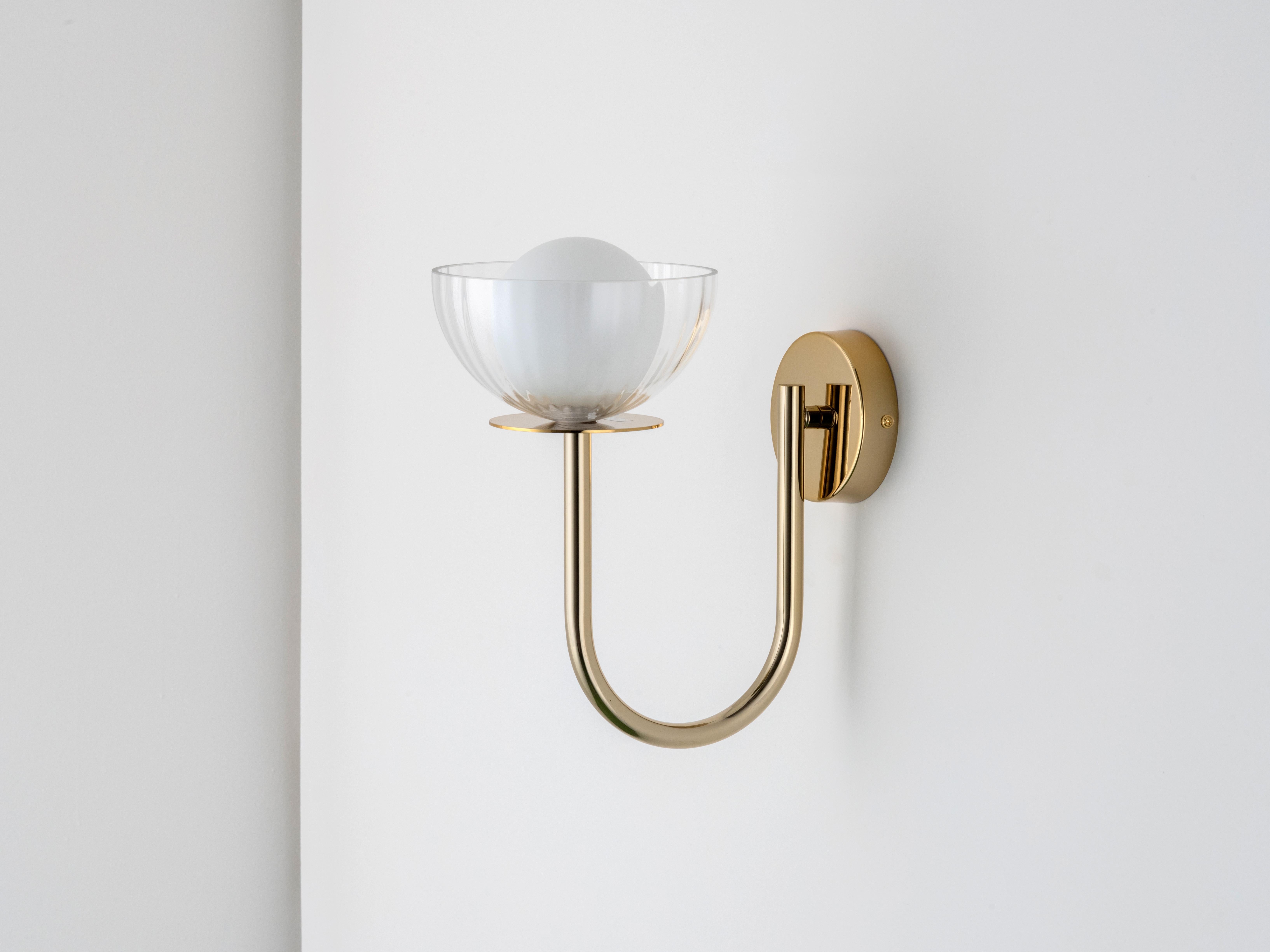 An elegant curved metal arm raises a clear ribbed glass bowl a top a luxurious brass plate to create this slender, space saving yet stylish wall mounted light. Within the bowl, our iconic opal orb glass shade, combining shapes and finishes into a