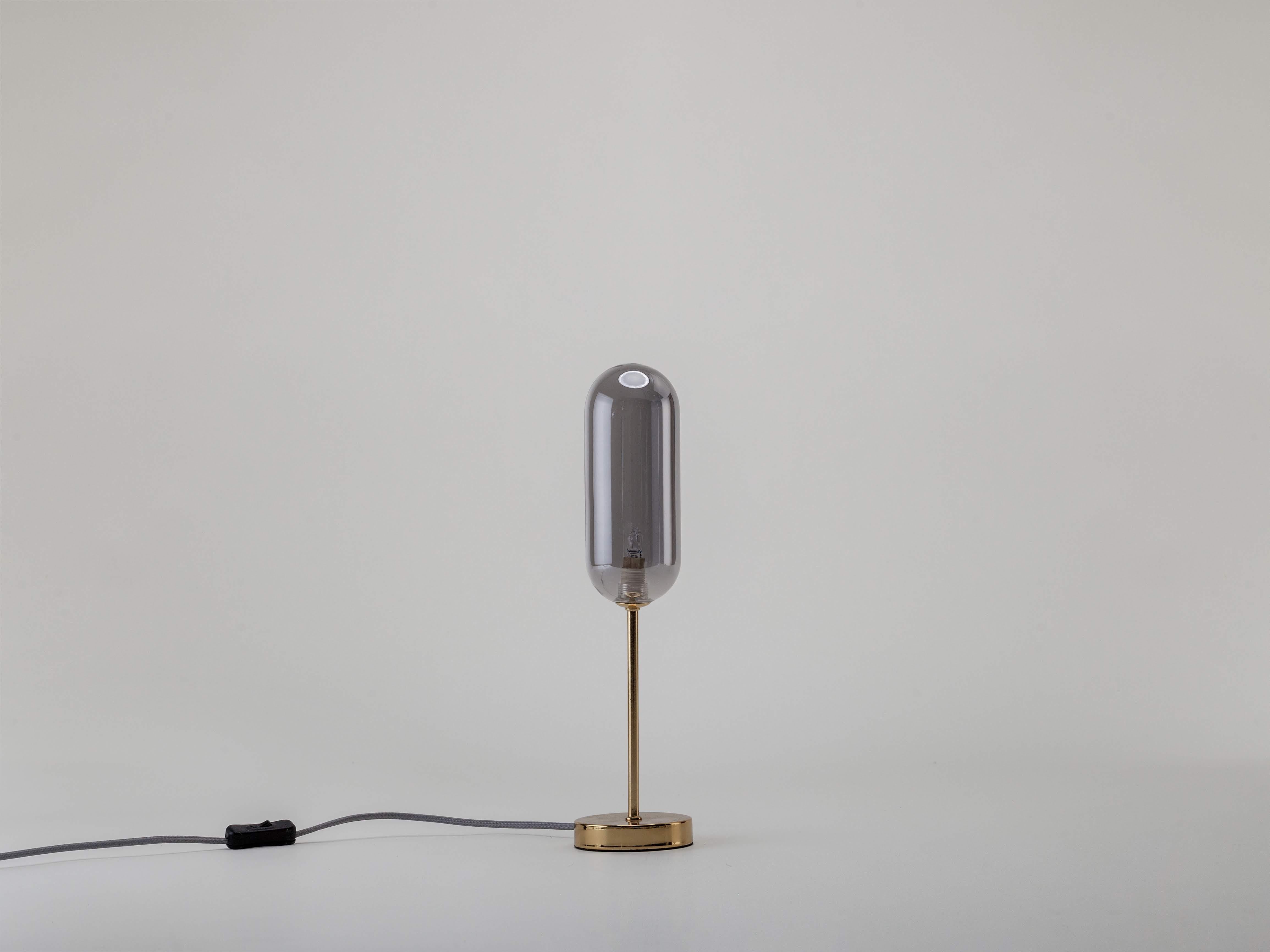 Contemporary and compact, this fun table lamp has all the style without the giant footprint, perfect for illuminating a room without taking up space. Moody smoked glass contrasts with the reflective brass arm and base for a stylish, modern design.