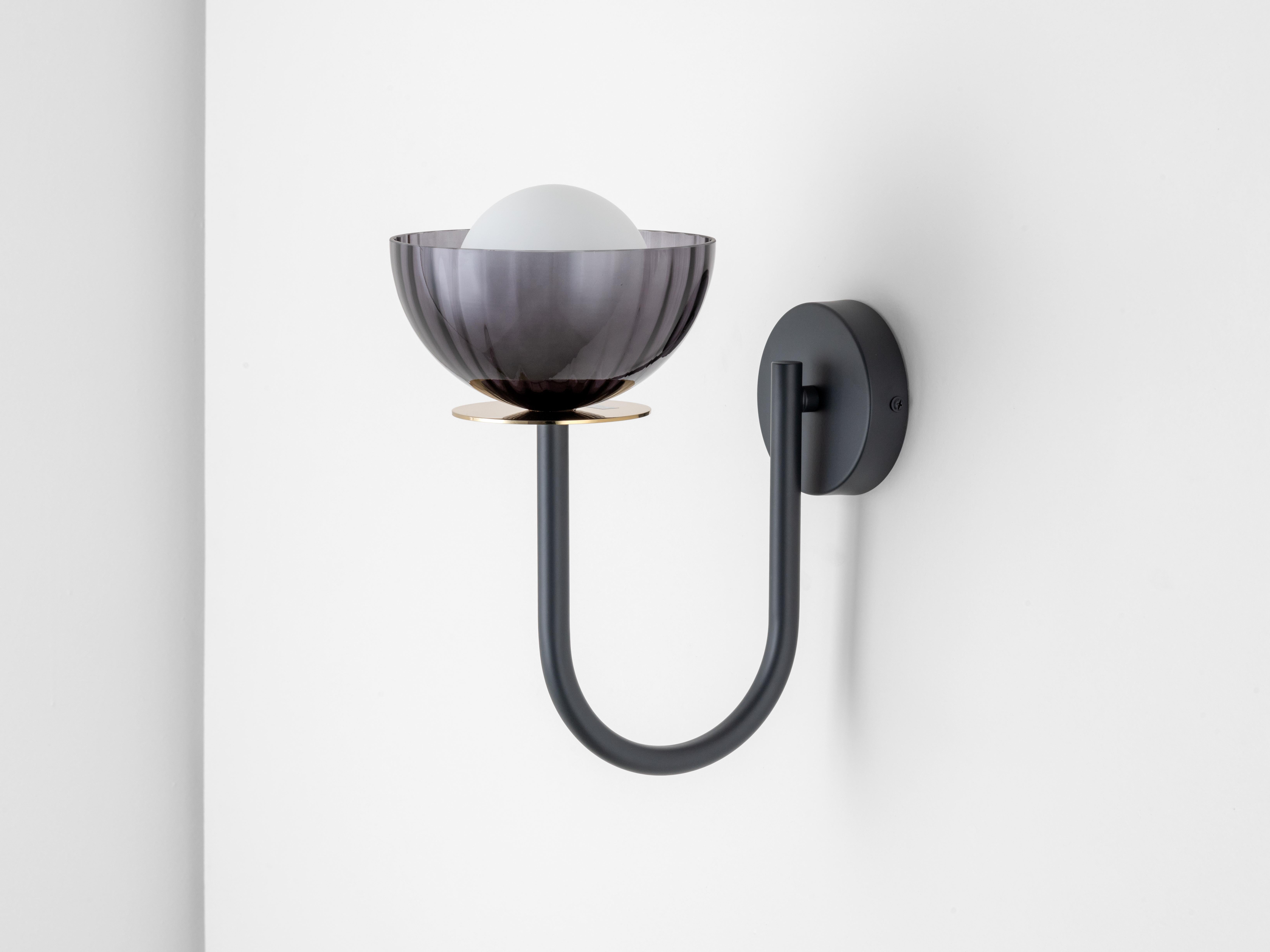 An elegant curved metal arm raises a smoked ribbed glass bowl a top a luxurious brass plate to create this slender, space saving yet stylish wall mounted light. Within the bowl, our iconic opal orb glass shade, combining shapes and finishes into a