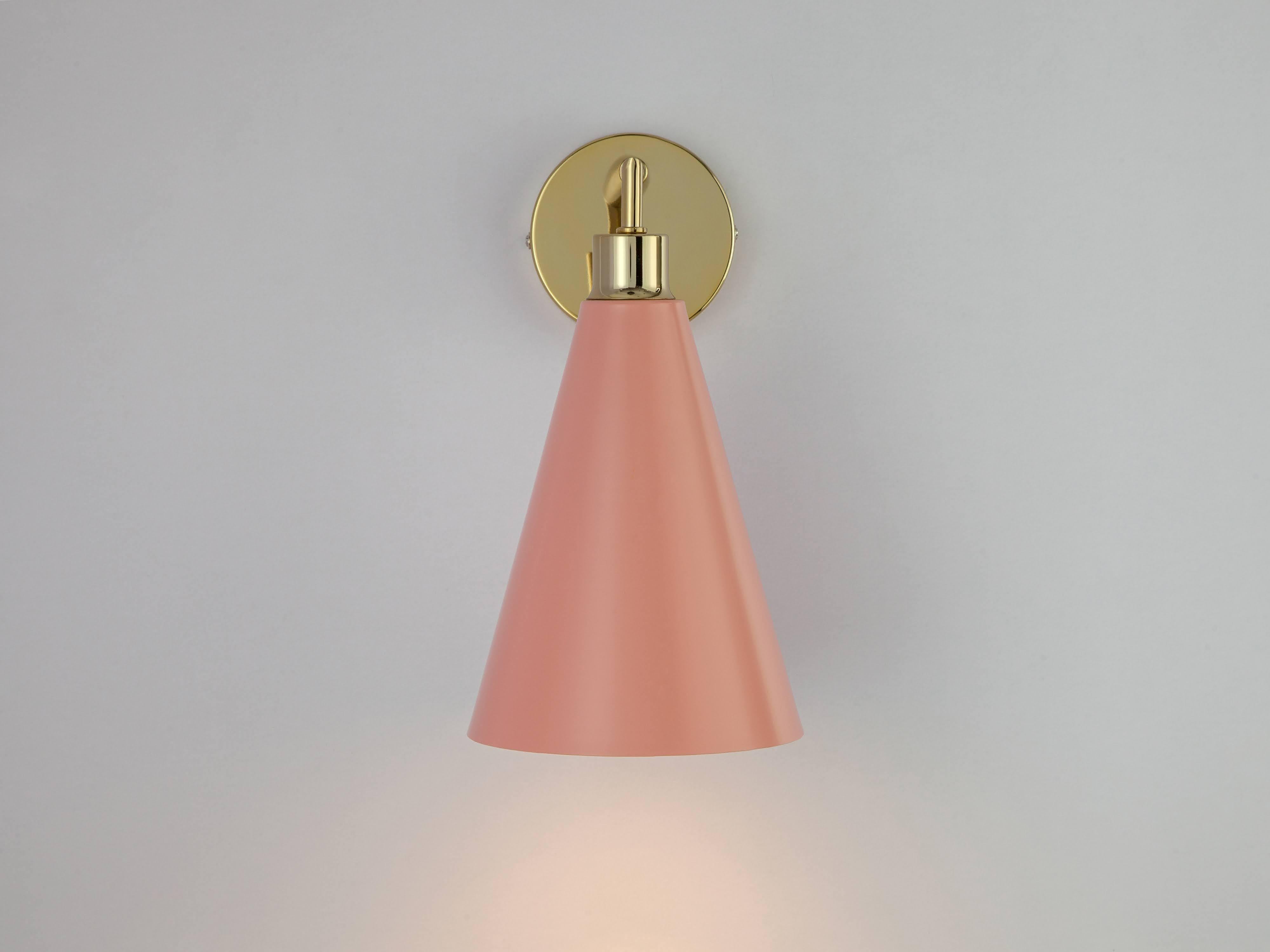 This sleek and practical wall sconce fuses traditional and contemporary. The stem base suspends an oversized cone shade which casts a wide atmospheric glow. Ideal for a living space or bedside light. Pink is a houseof staple; a popular colour pop in