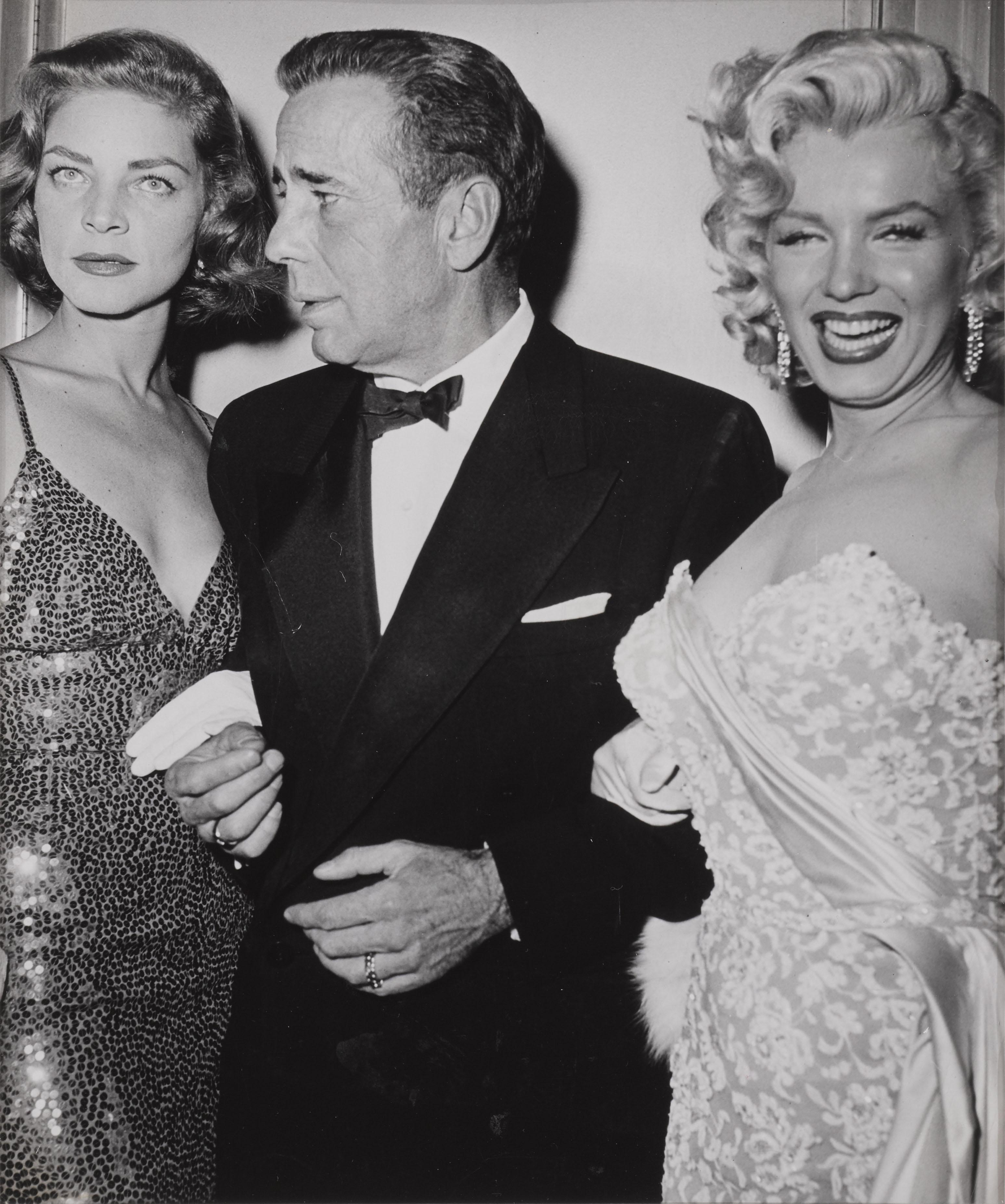 Original-Candid-Foto von 1953  mit Humphrey Bogart zwischen Marilyn Monroe und Lauren Bacall bei der Premiere von How to Marry a Millionaire .

Auf der Rückseite befindet sich eine Plexiglasscheibe mit Fotoinformationen und Datumsstempel vom 4.