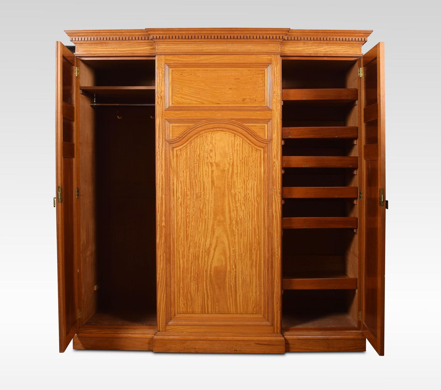 Howard and Sons satinwood breakfront combination wardrobe, having flared cornice with dentil mouldings. Above a centre door with rectangular panel over an arch panel, flanked by a pair of three-panel doors opening to reveal fitted interior. The