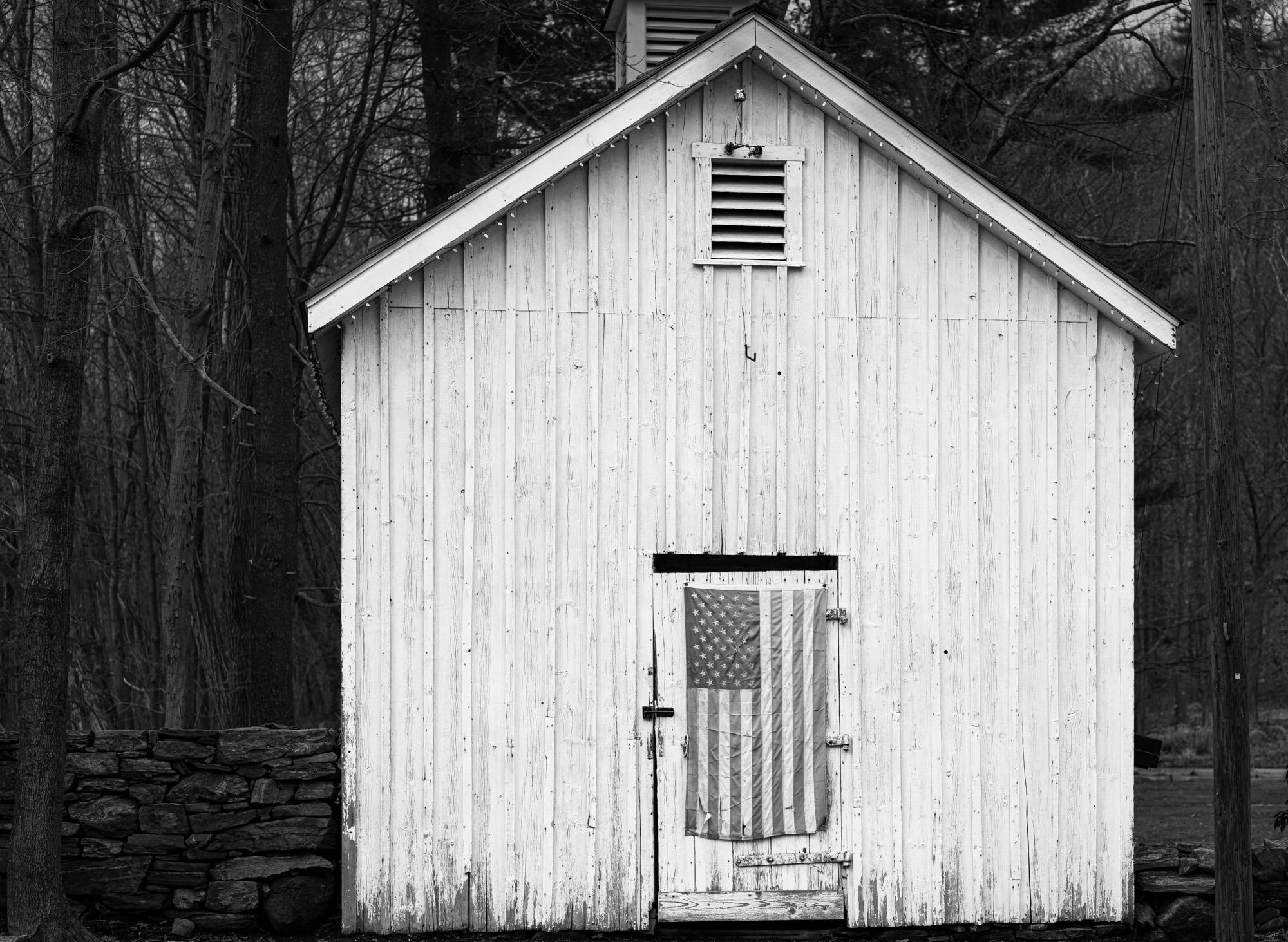  Limited Edition Black and White Photograph - "American Barn", 2022. The American flag has a variety  of symbolic meaning these days. This flag has seen better days but it matches the barn rather well.

About Howard Lewis:
Lewis’ artistic practice