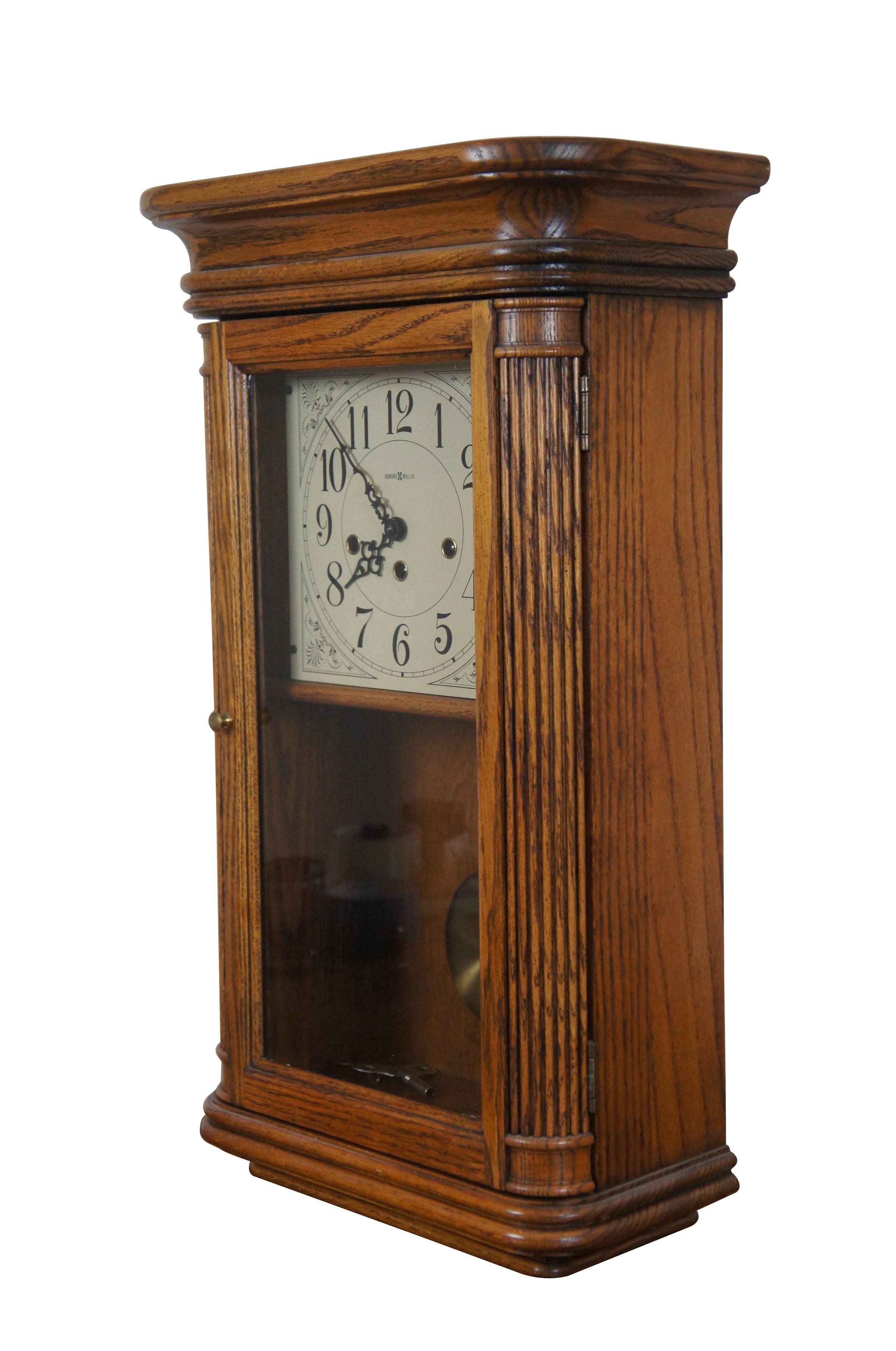 Vintage Sandringham wall clock by the Howard Miller Clock Company, Model 613-108, hand wound, Westminster chime, Yorkshire Oak. Molded base and flared pediment with rounded corners, fluted columns flanking the glass front with pendulum, off white
