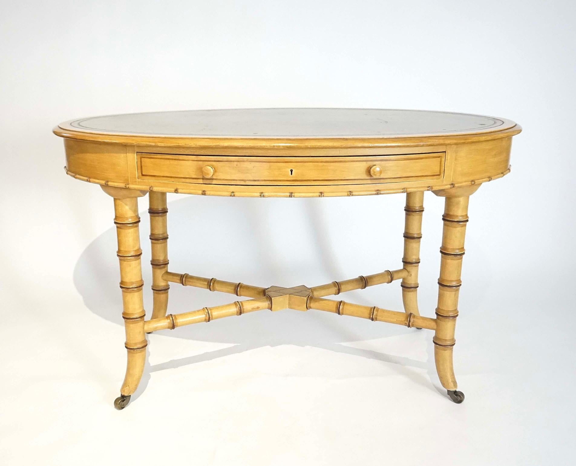 English circa 1875 Aesthetic Movement writing table or desk by London cabinetmakers Howard & Sons having original green leather top; the oval form case with single drawer and original faux bamboo painted finish on turned segmented x-form stretcher