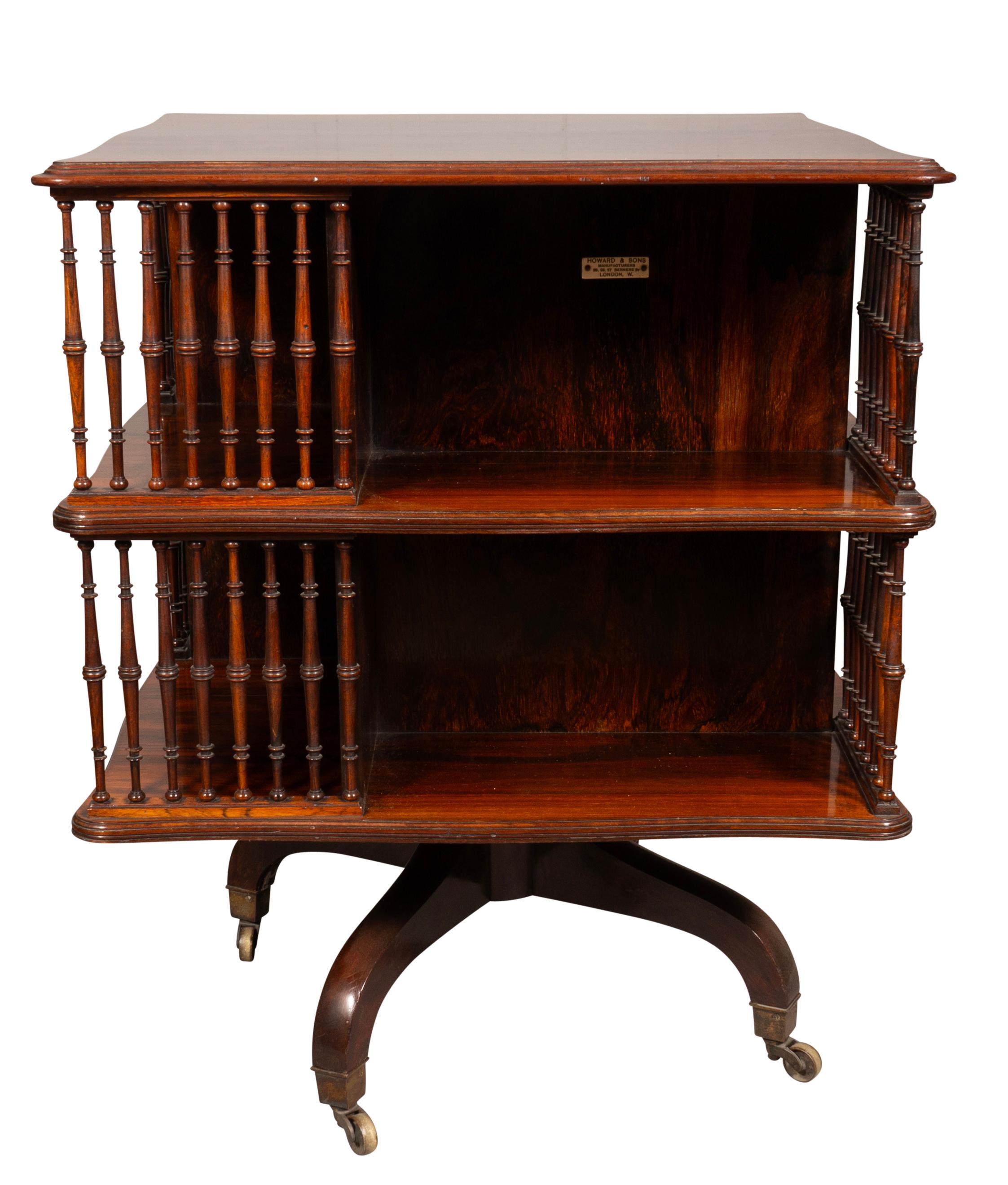 Square with serpentine edge. conforming lower shelf with spindles and book storage. Raised on saber legs and casters. Signed in celluloid plaque Howard & Sons. London.