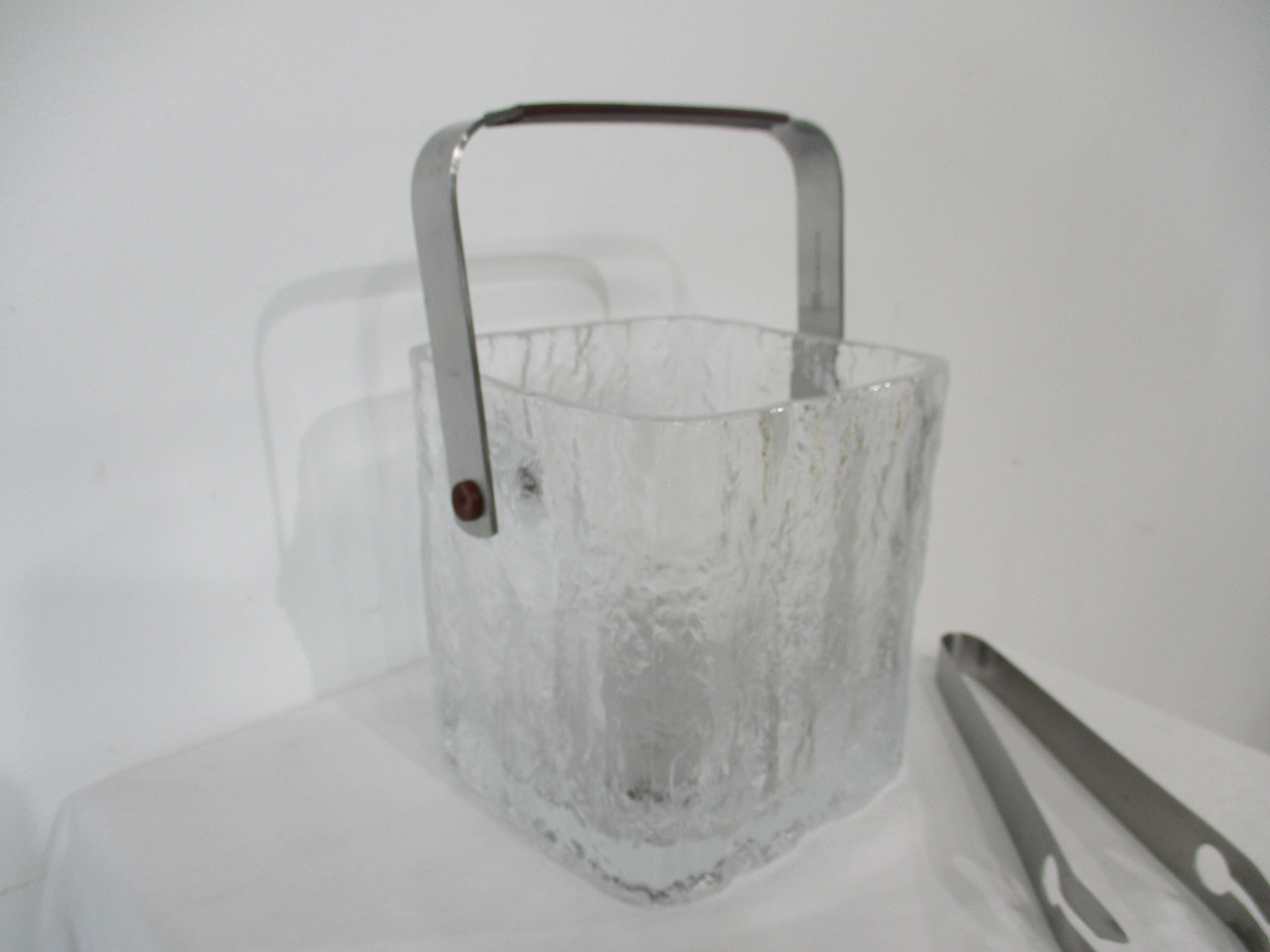A molded glass ice bucket in the glacier style with the look of frozen ice , having a stainless steel handle , matching tongs and bottom strainer . The perfect size for that built in bar or countertop , crafted in Japan by the Hoya Glass company . 
 