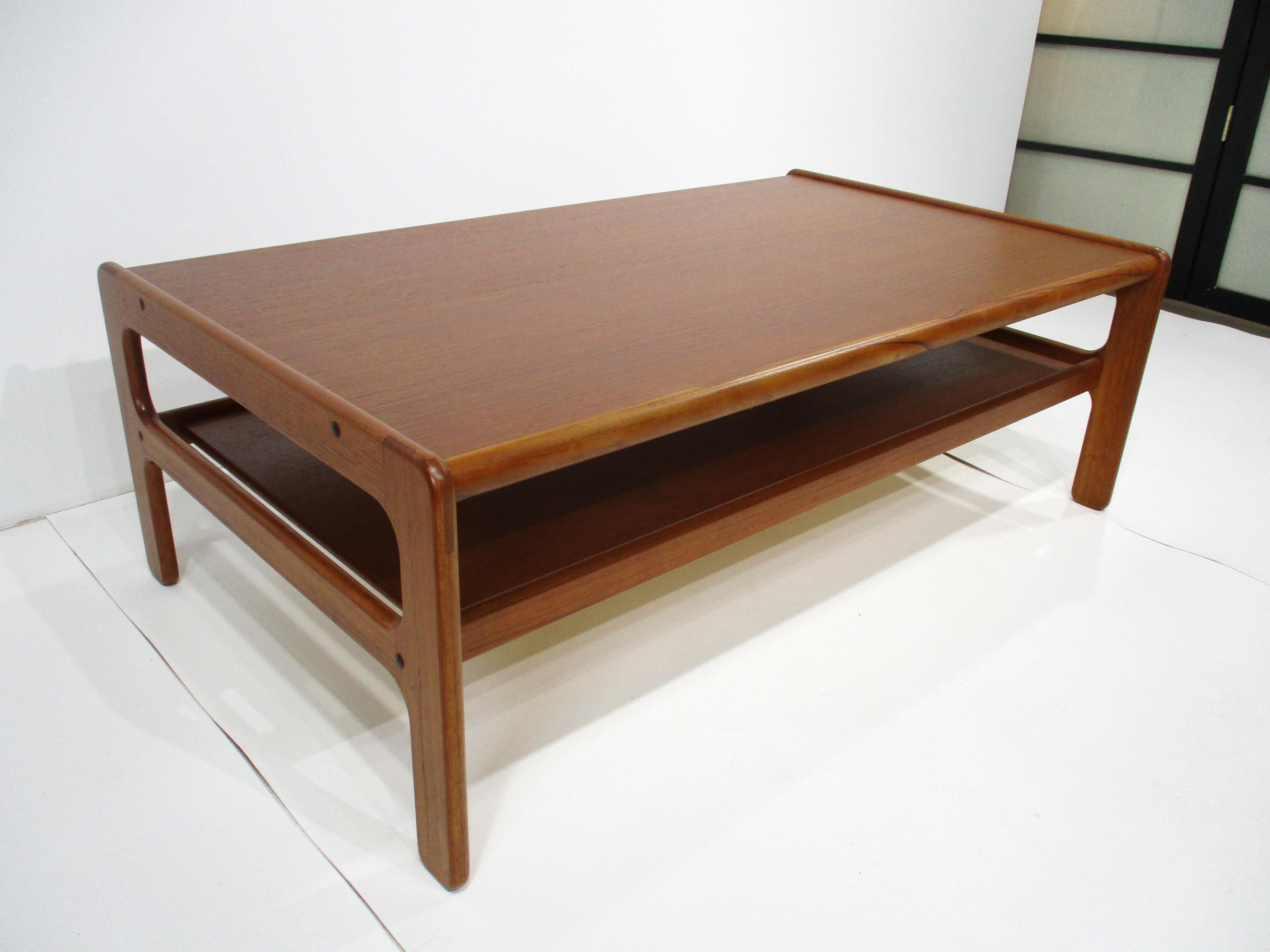 A larger sized teak wood coffee table with lower functional shelve having soft edge design . Manufactured in the manner of Dyrlund and H.P. Hansen with ink stamp to the bottom made in Denmark .  
