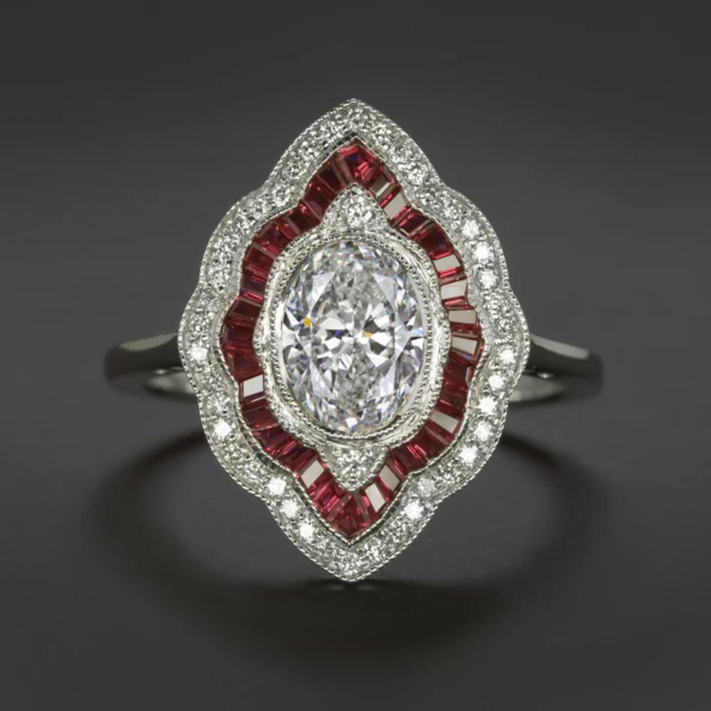 This diamond and ruby ring showcases a stunning Art Deco style design, combining rich color with substantial sparkle. 
At the heart of this piece is a vibrant 1.00 carat oval cut diamond, HRD certified, graded H SI2, and displaying a bright white