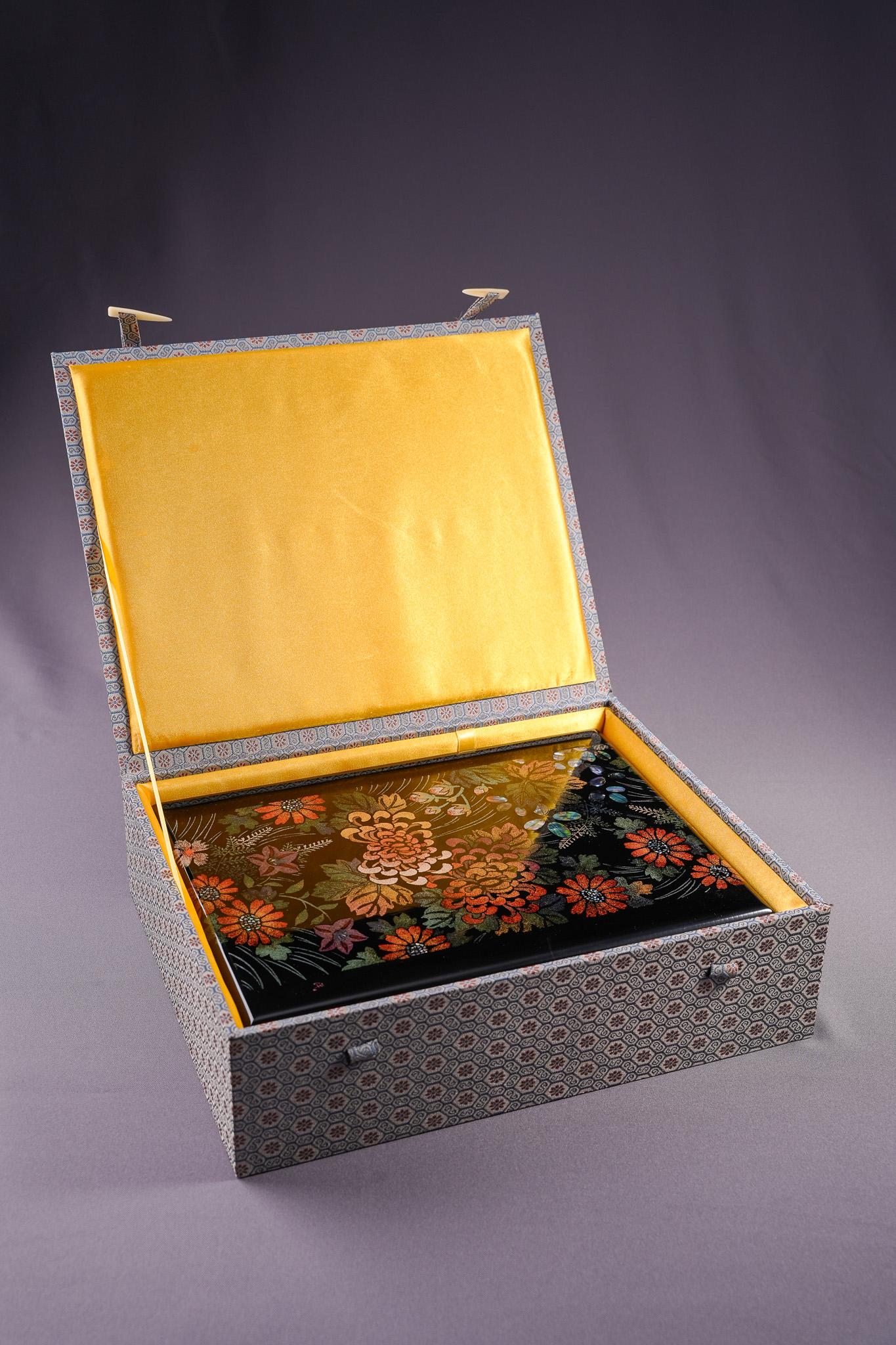 Diese Lackschatulle von Hsien Min Wang zeigt ein Chrysanthemenmotiv, das die heitere Schönheit des Herbstes einfängt. Die Dose wird mit der Technik des Formlacks geformt und mit einer Schichtlackierung und poliertem Maki-e veredelt. Die