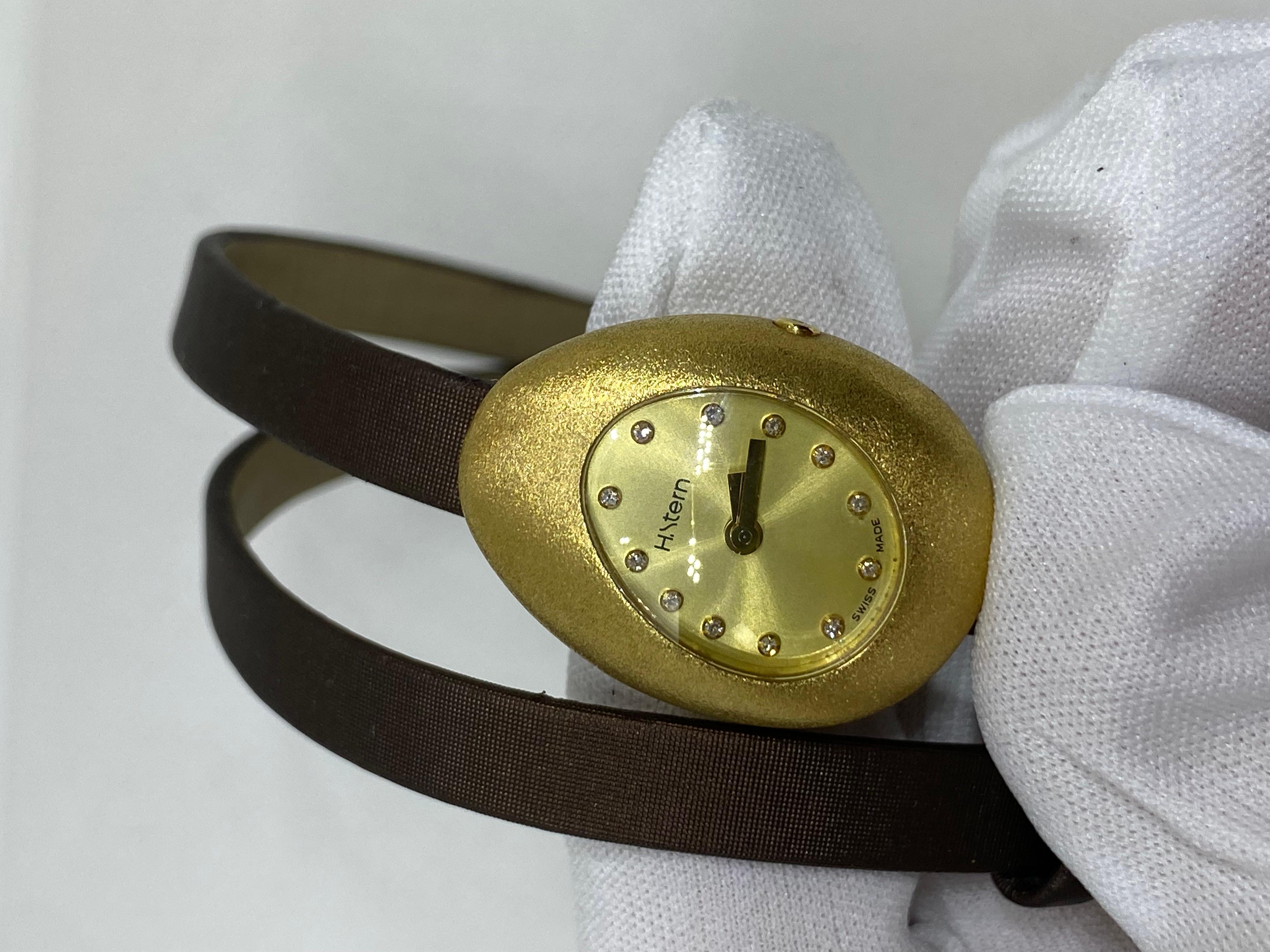 18K yellow gold 21mm x 29mm x 12mm. H. Stern Golden Stones watch featuring a quartz movement, brushed matte bezel, champagne dial and brown satin wrap strap with tang buckle. Swiss made. 3 ATM Waterproof.
