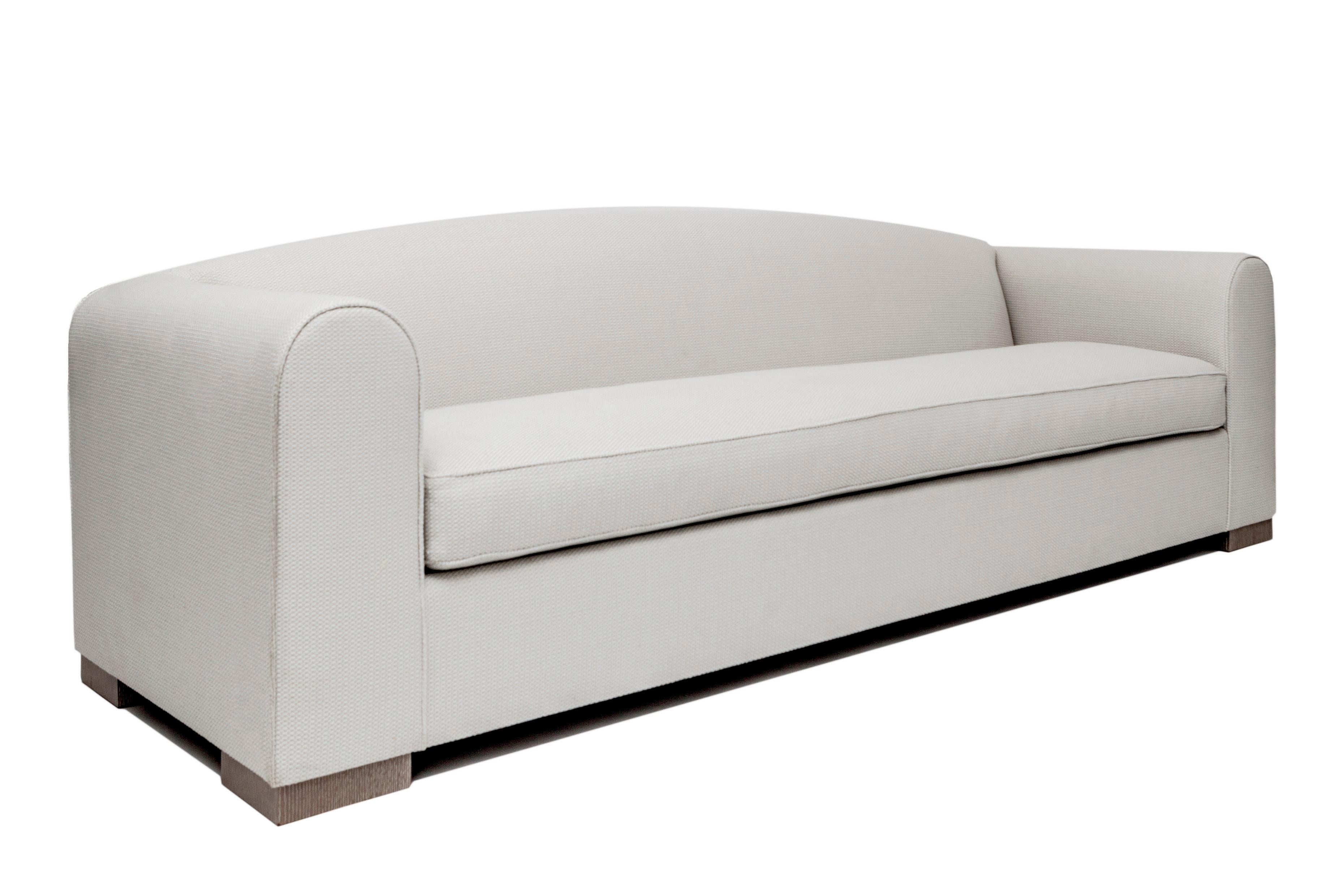 Arched, tight back sofa with wide, curved top arms and bench seat cushion. The Hubert sofa frame is constructed using solid maple wood with 50 / 50 down feather filled cushions. Four finishes available for sofa legs. Available in four cotton fabric