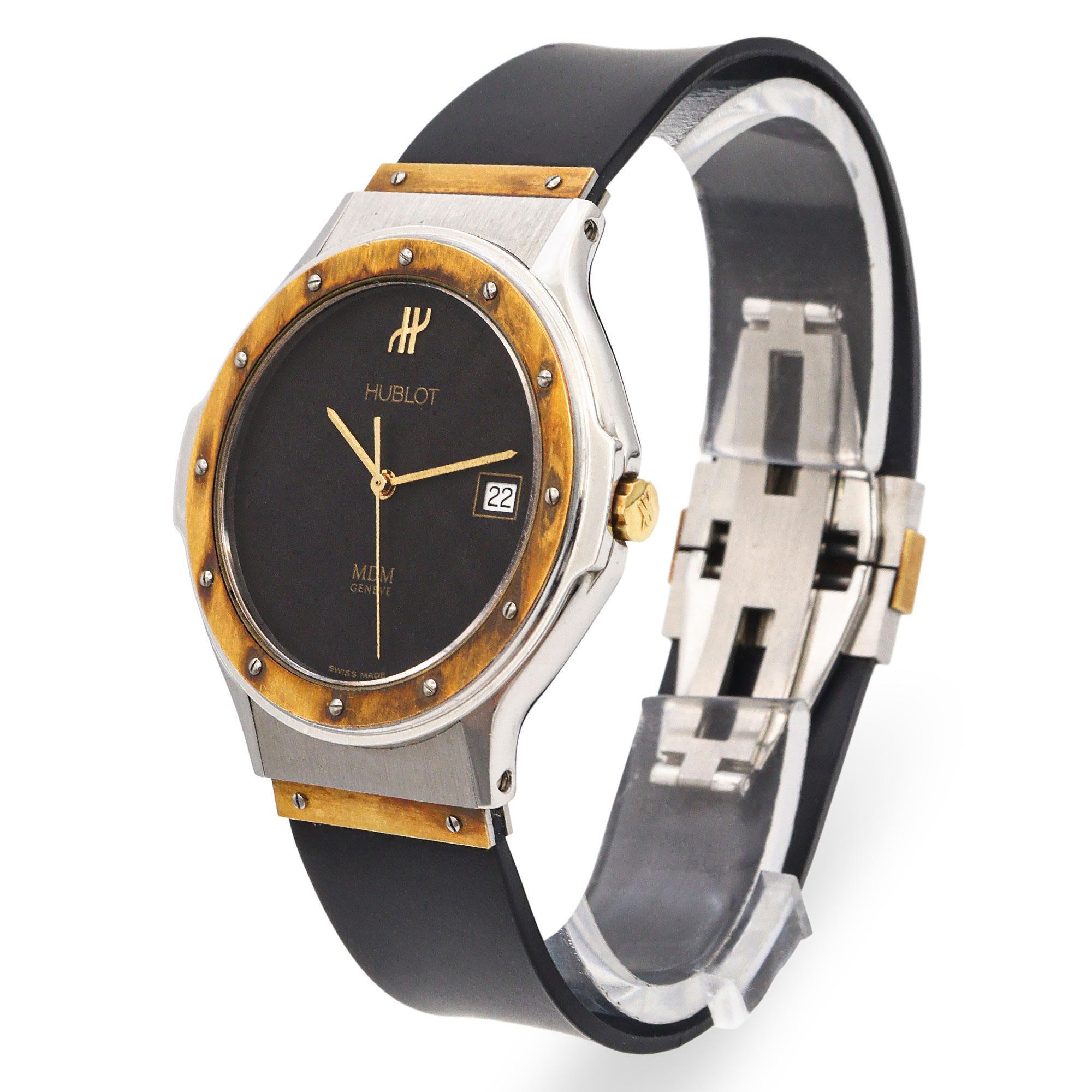 Diese elegante und raffinierte Hublot Classic MDM Genève Date Quartz Herrenuhr verkörpert die für die Marke typische Mischung aus Eleganz und Innovation. Das Gehäuse aus gebürstetem Edelstahl ist mit einer markanten goldfarbenen Lünette versehen,