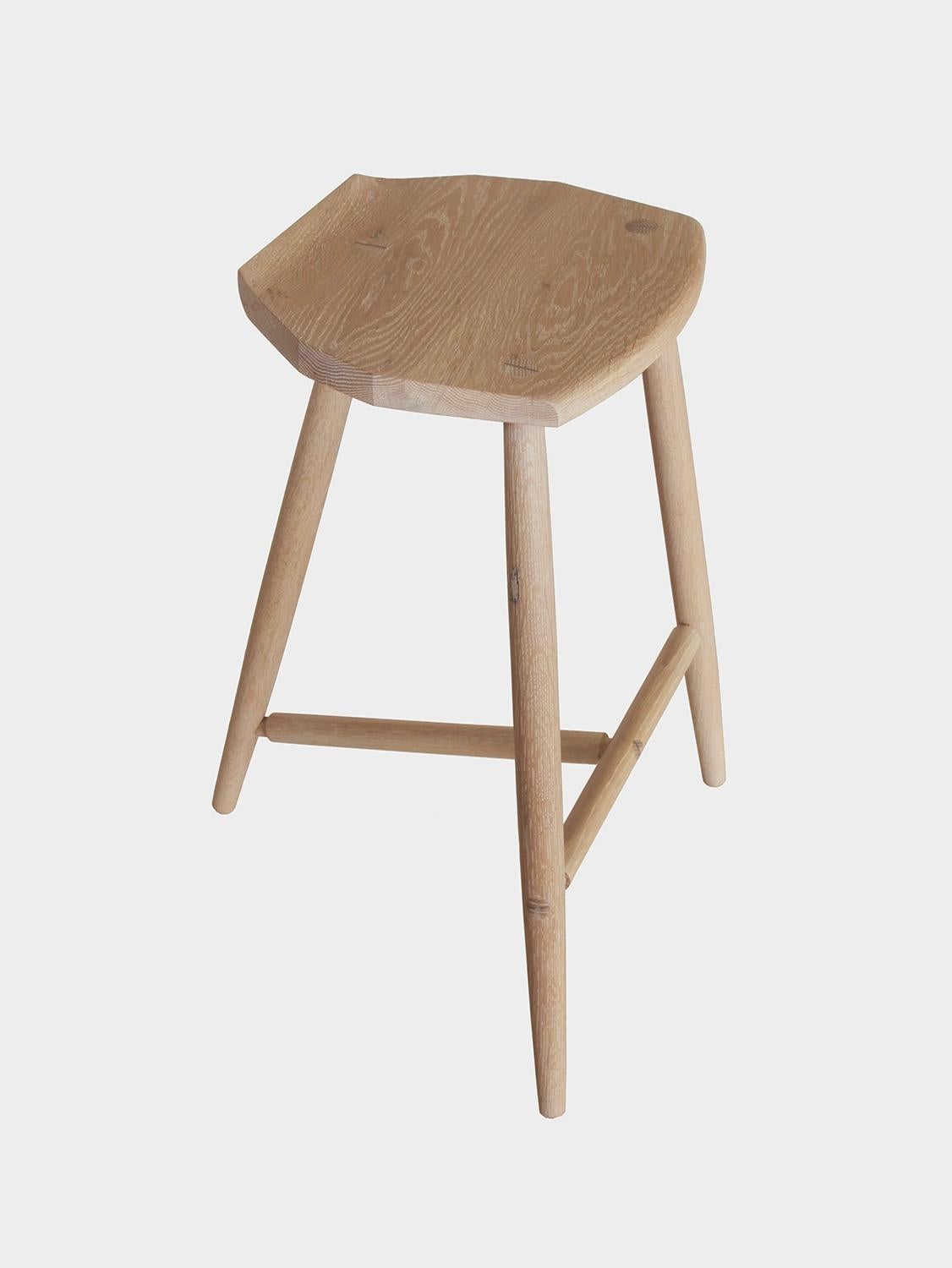 New York Heartwoods' cerused oak solid wood counter height Jordan stool is influenced by Shaker and Mid-Century design; created to be comfortable, lightweight and easy to move; and features three turned legs, a unique hand-carved faceted seat, and