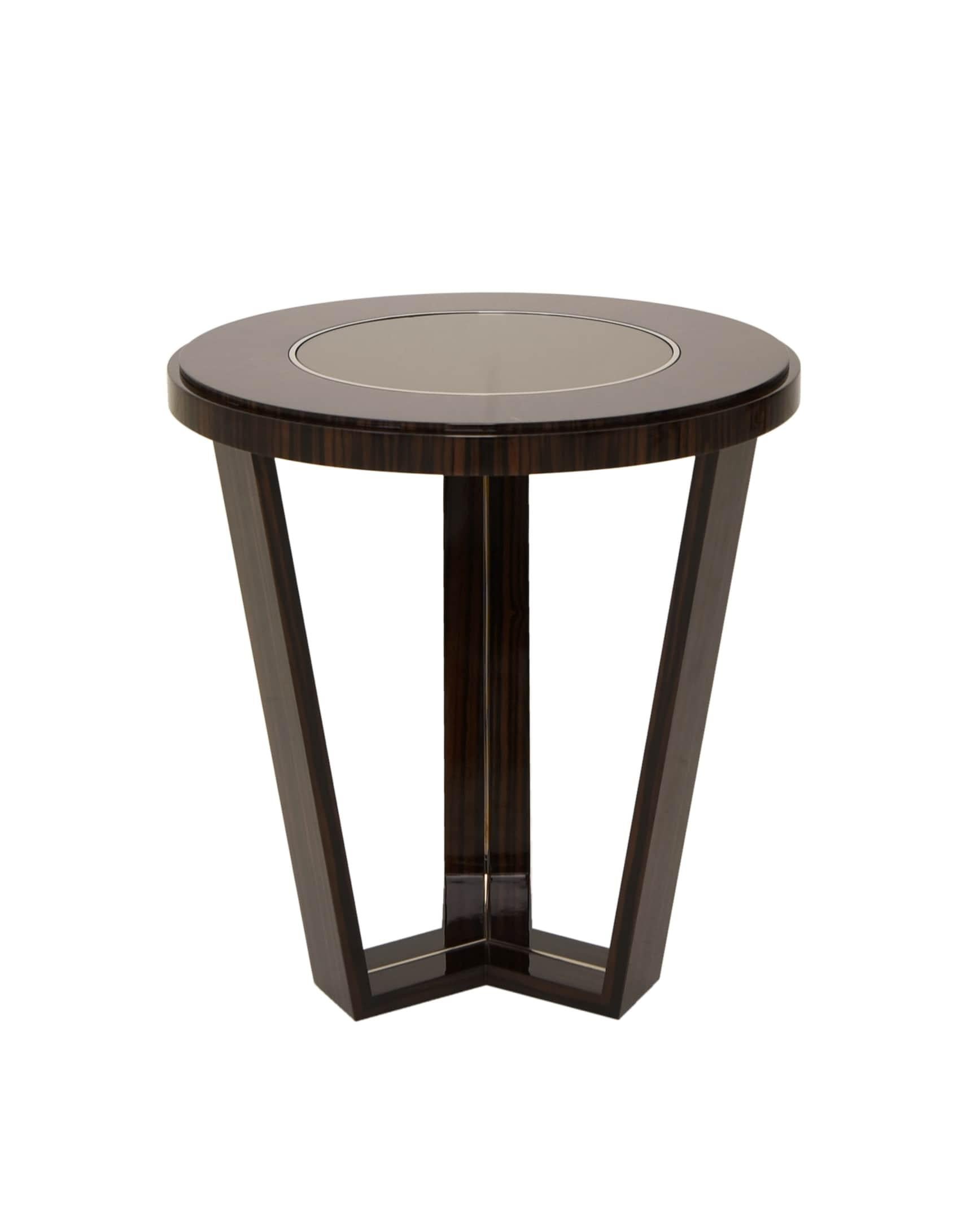 Cette table d'appoint combine la chaleur du bois Canela Noir avec l'élégance subtile des incrustations en laiton brossé. Son design se définit par trois pieds reliés entre eux, supportant un plateau rond en bois, métal et verre. La dualité des tons
