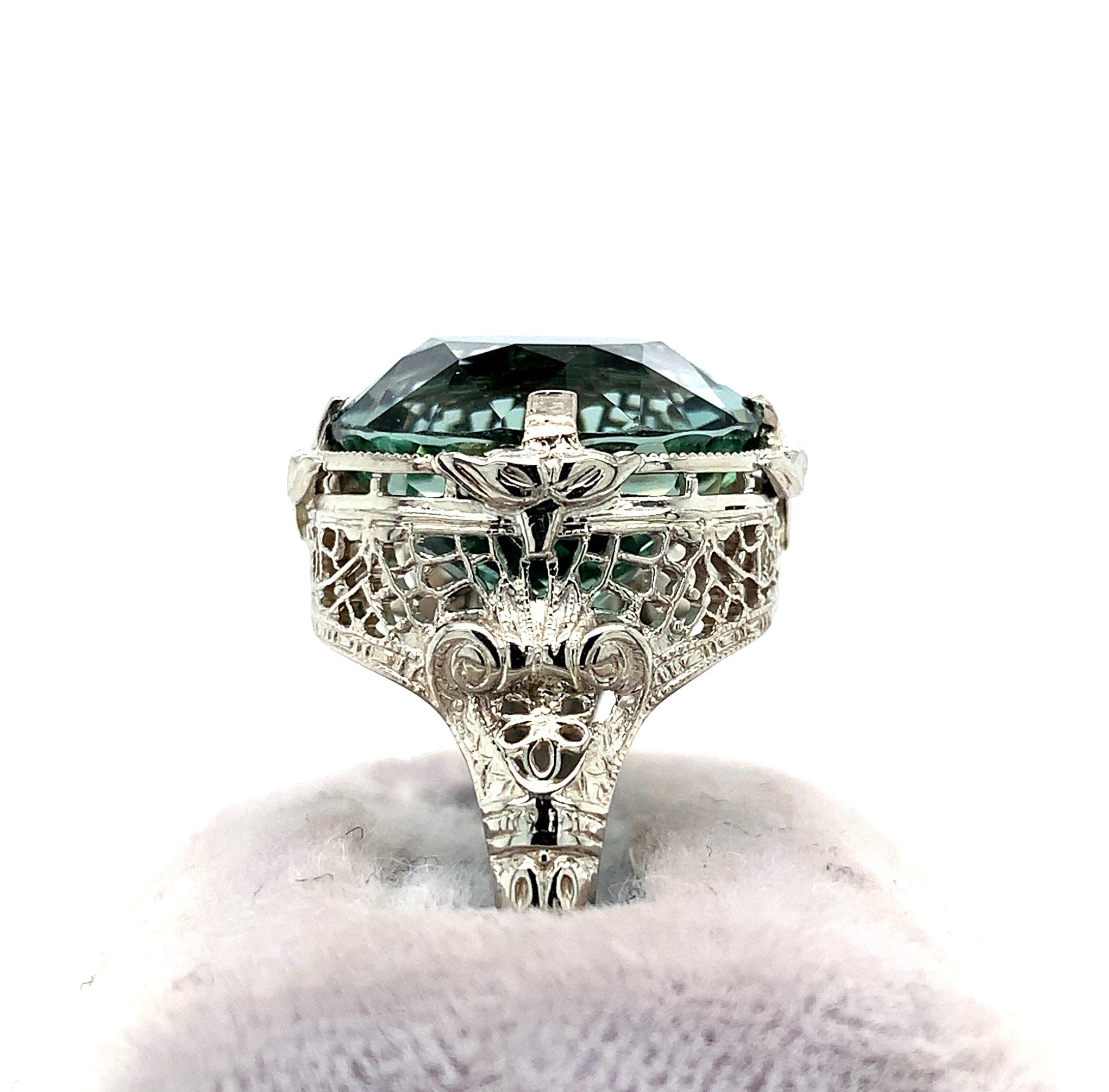  14K white gold filigree ring featuring a huge green tourmaline weighing 12.21 carats. The tourmaline has a blue-green teal color. It is oval brilliant cut with extra faceting and measures about 15mm x 12mm. The ring fits a size 8 3/4 finger and