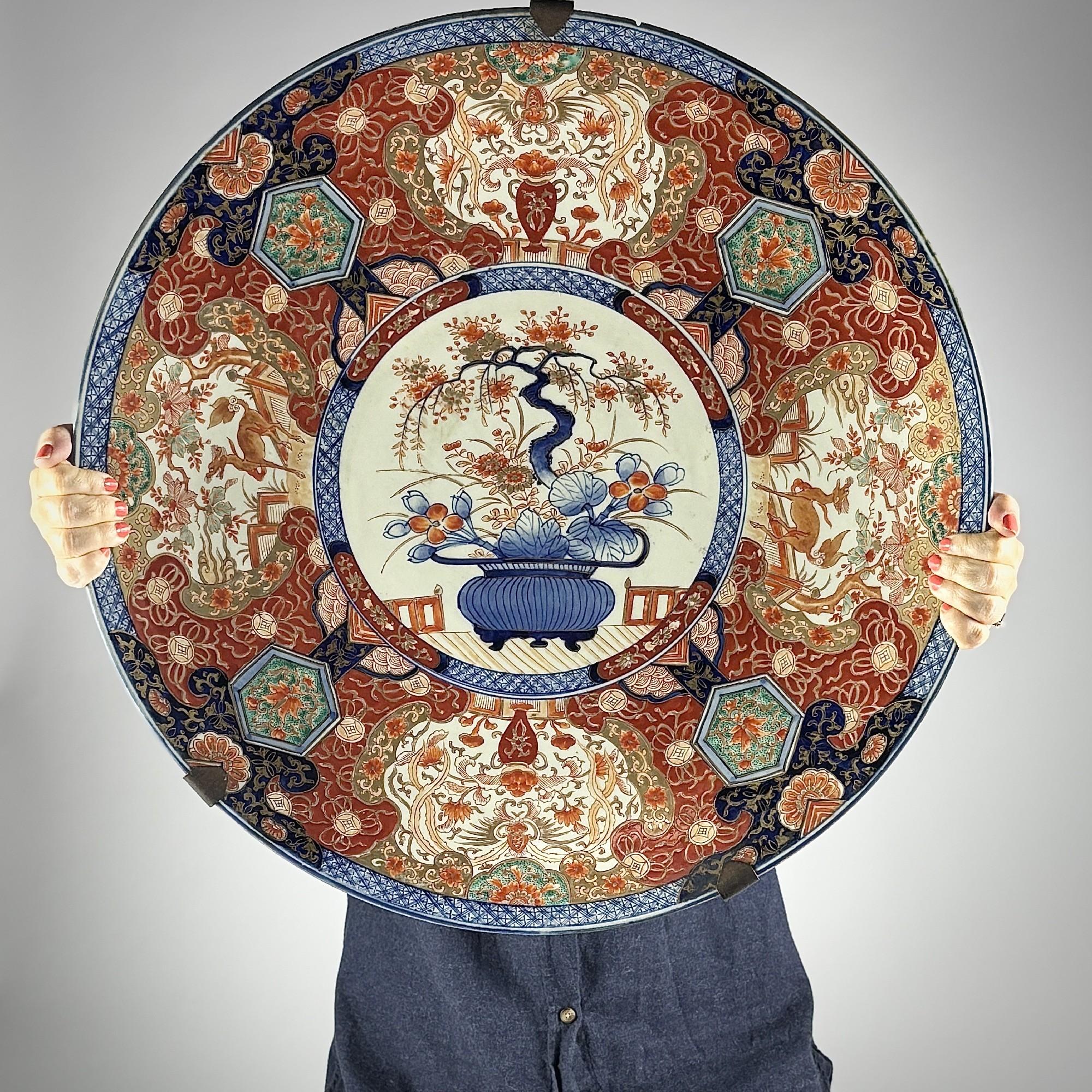 Huge Japanese Imari Charger, Meiji Period (1868 - 1912) The centre painted flower and Bonsai filled Jardiniere, the cavetto painted with four grand cartouches. The reverse also decorated, bespoke 20th Century hanging Bracket. Japan, Circa 1890.