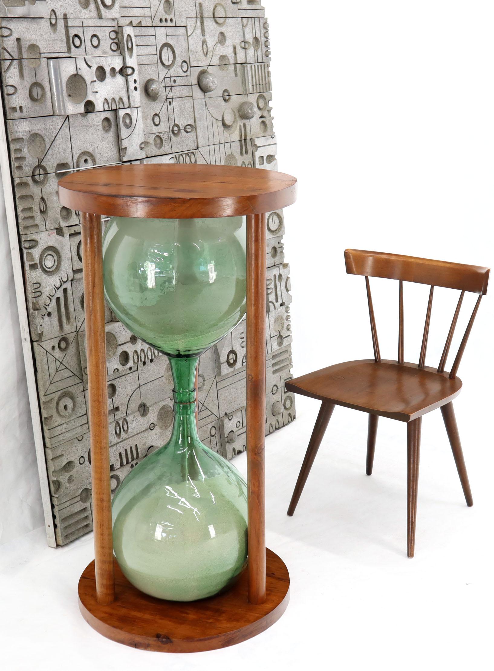 Artist-signed and dated (Hudson Favell 1979) huge sandglass pedestal table timer. Two heavy blocks slabs of wood holding together two greenish art glass jars filled with sand. Mid-Century Modern design concept. Measures: huge 22” diameter, 44” tall.