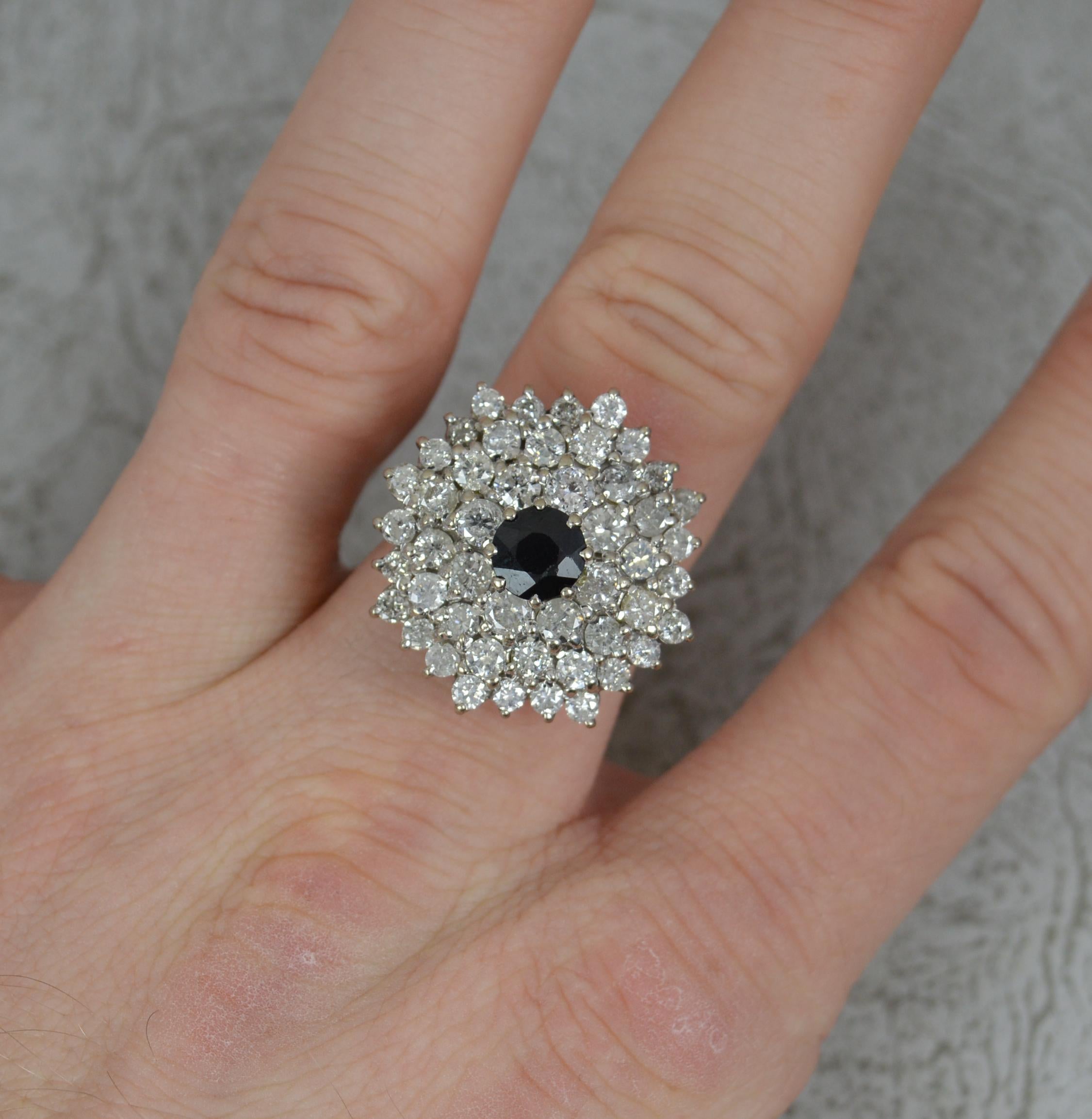 A stunning sapphire and diamond cluster ring.
Solid 18 carat white gold shank and setting.
Designed as a four tier cluster head. The hexagonal head is set with a round cut dark blue sapphire to centre with graduated round brilliant cut diamonds