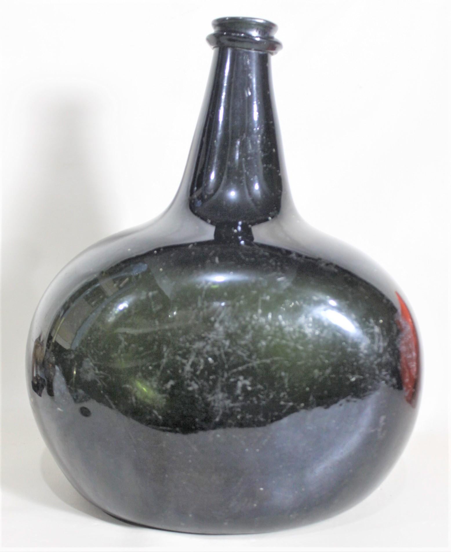 This very large and substantial antique wine bottle's exact origins are unknown, but it is presumed to be English or possibly Dutch and dating from the early 1700's. The bottle was hand blown and formed and uses a very thick deep olive green glass.