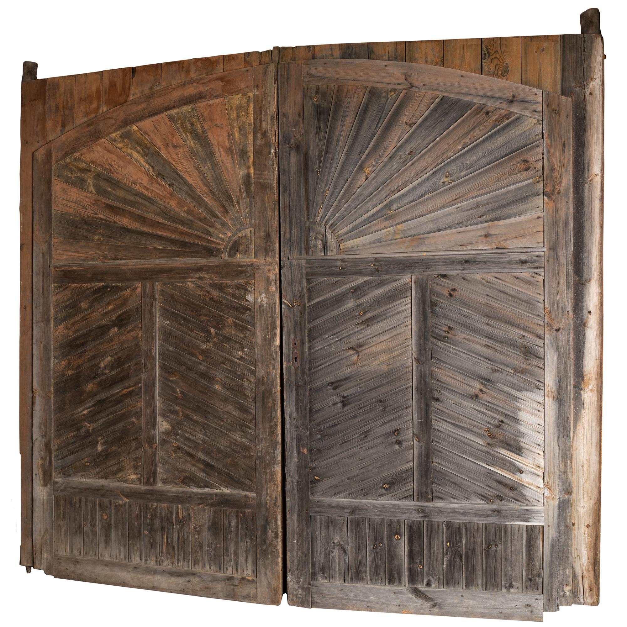This large pair of doors make an impressive architectural statement standing 10' tall with a sunburst pattern in the upper section. Within the center of the sun pattern you see the monogram of HS. The worn patina of the grey weathered wood adds to