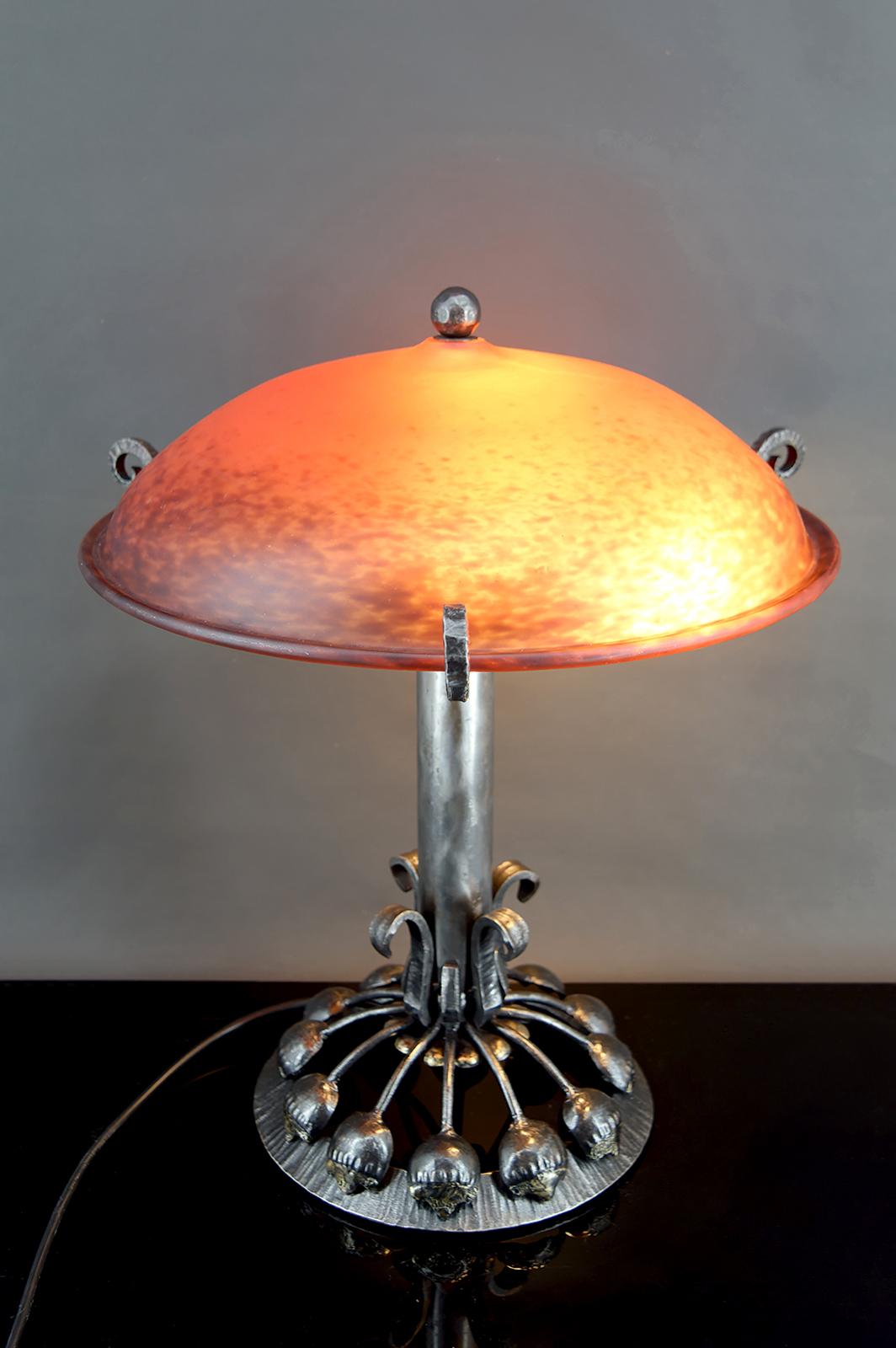Importante Lámpara Art Decó con Soporte de Hierro Forjado Botánico Estilizado y Cúpula de Vidrio Jaspeado Rojo-Naranja, Francia, Circa 1930

Elegante y rara, esta majestuosa lámpara Art Déco presenta una estilizada montura botánica de hierro