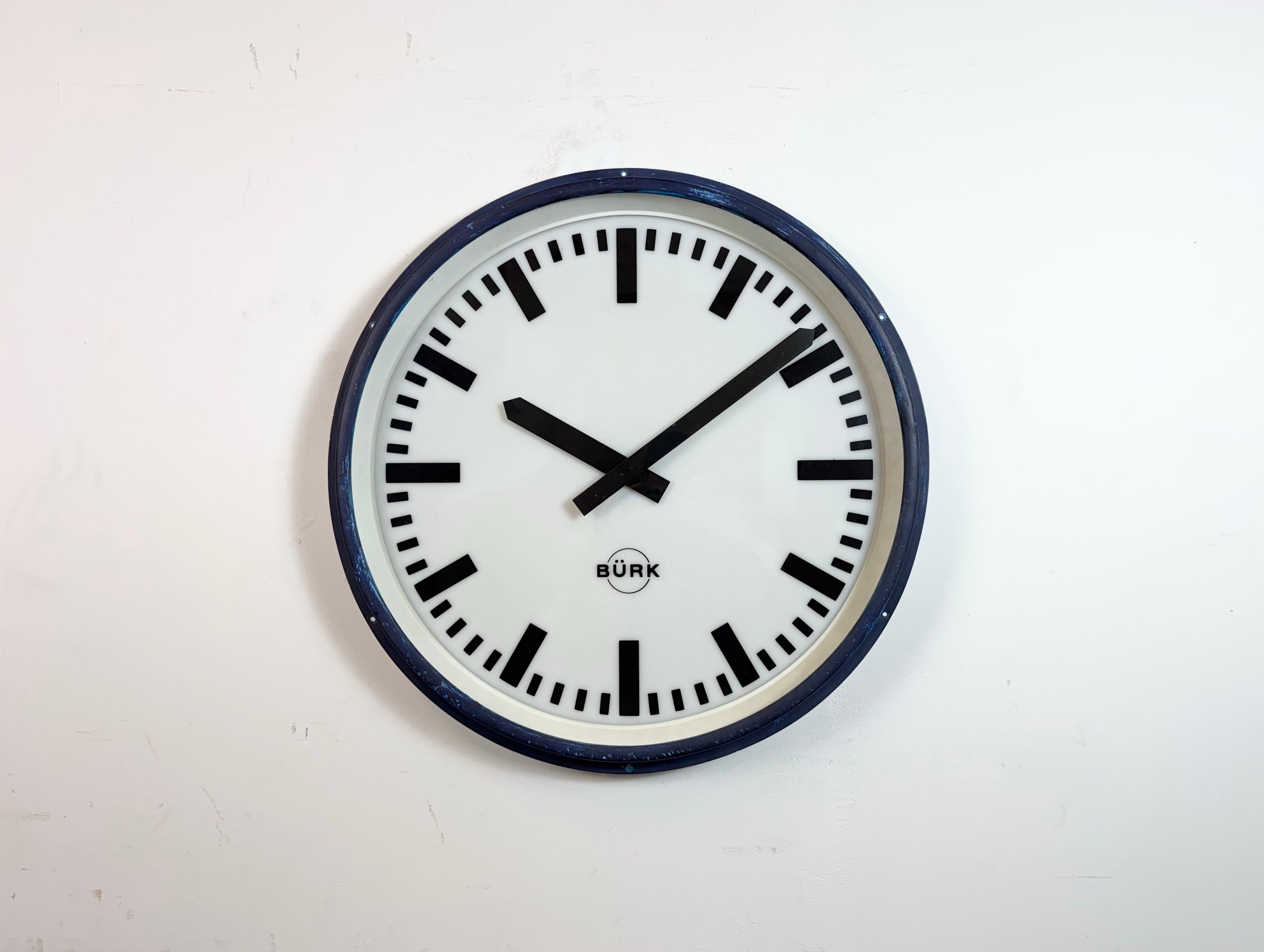 Vintage factory Burk wall clock made in Germany during the 1960s. It features a blue iron frame, a plastic dial, an aluminium hands and a clear glass cover. The piece has been converted into a battery-powered clockwork and requires only one