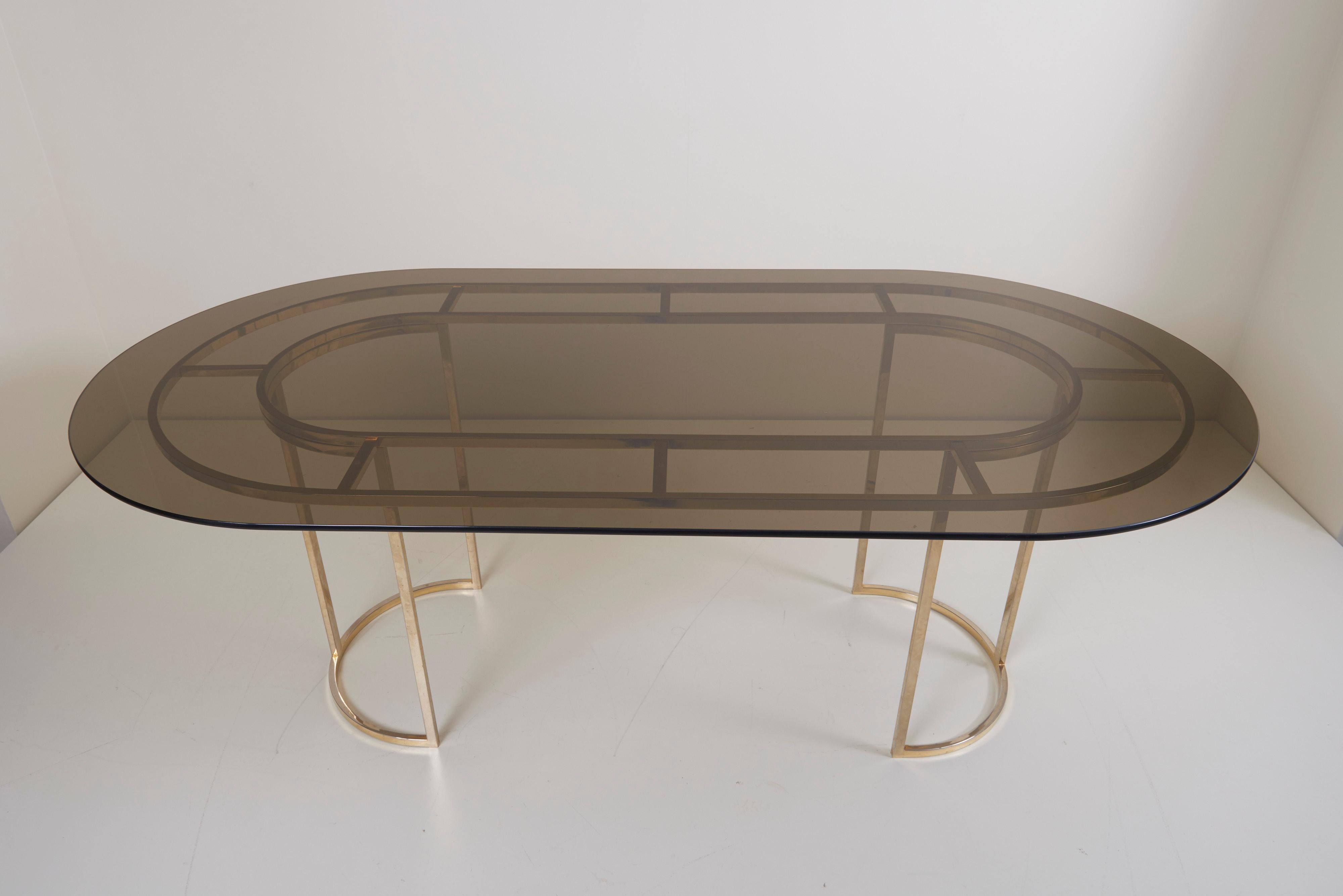 Beautiful large dining table in brass with a tinted glass table top in the style of Romeo Rega. The table is in a very good condition. A set of matching chairs is also listed.