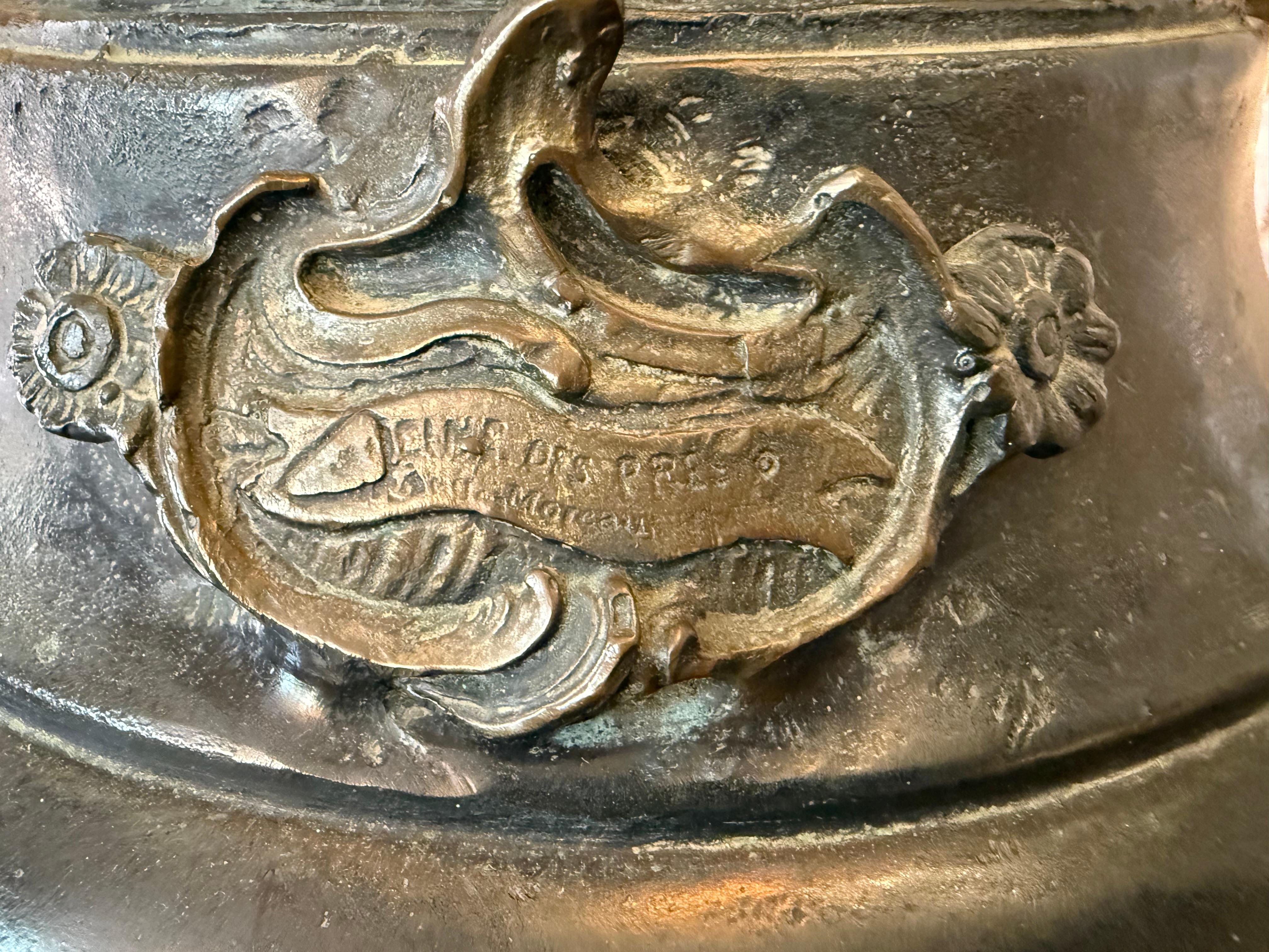 Il s'agit d'une lampe sculpture en bronze de A.Moreau. Elle représente une jeune paysanne vêtue d'une longue robe, pieds nus, debout sur un petit talus fleuri et tenant à deux mains des abat-jour en forme de fleurs de lys en verre translucide. Un