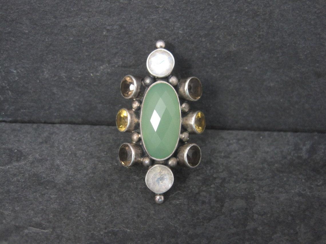 This gorgeous sterling silver ring is a product of Nicky Butler's RAJ collection.
It is limited edition #32 of 2000.

This ring features a stunning 10x20mm green chalcedony accented by 2 round 7mm rainbow moonstones, 4 round 6mm smoky quartz and 2