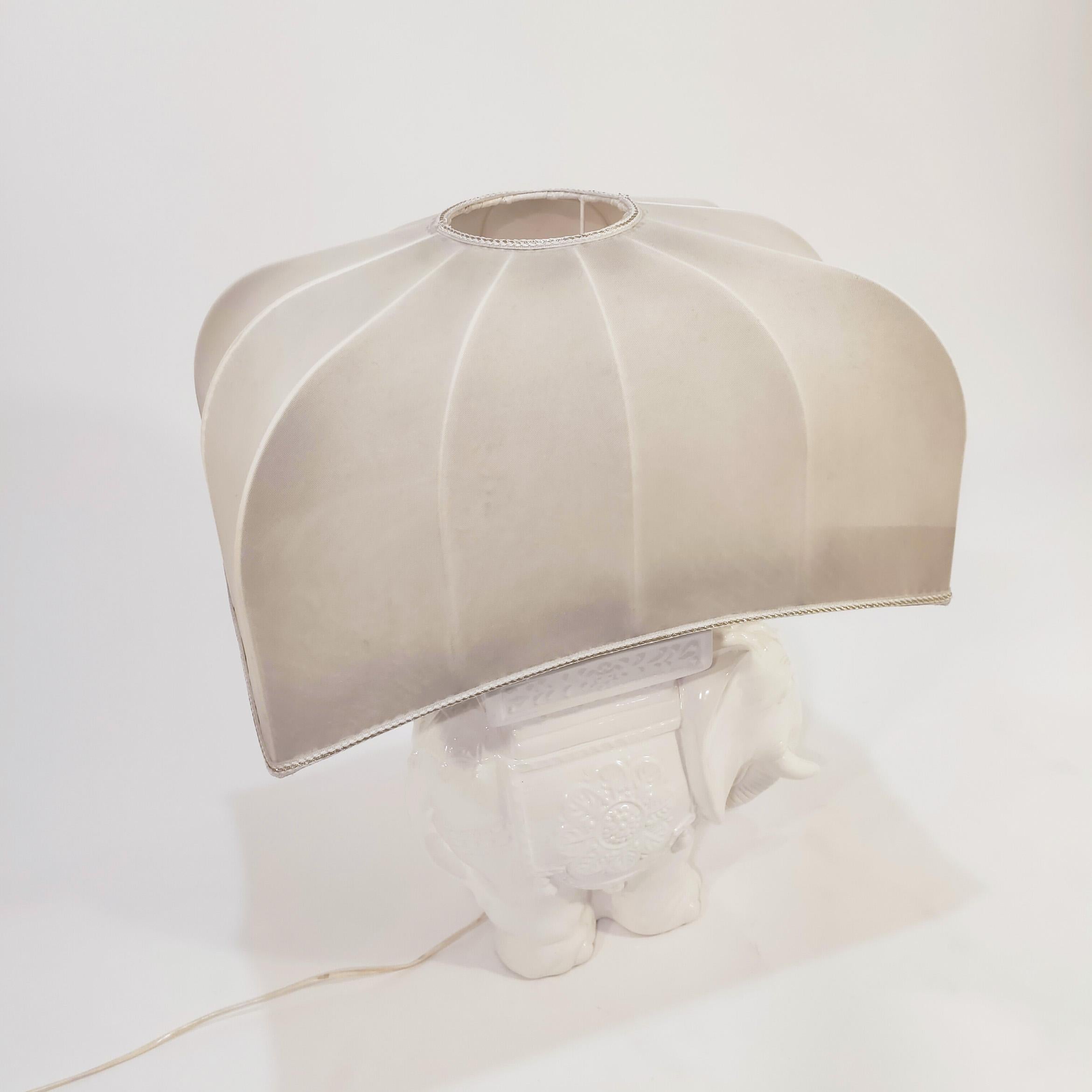 Large desk or table lamp from the Spanish brand Cetres, 1970s. Glazed white ceramic body in the shape of an Indian elephant with floral reliefs and matching original textile shade. This tiype of piece was very popular during the 70s and 80s in some