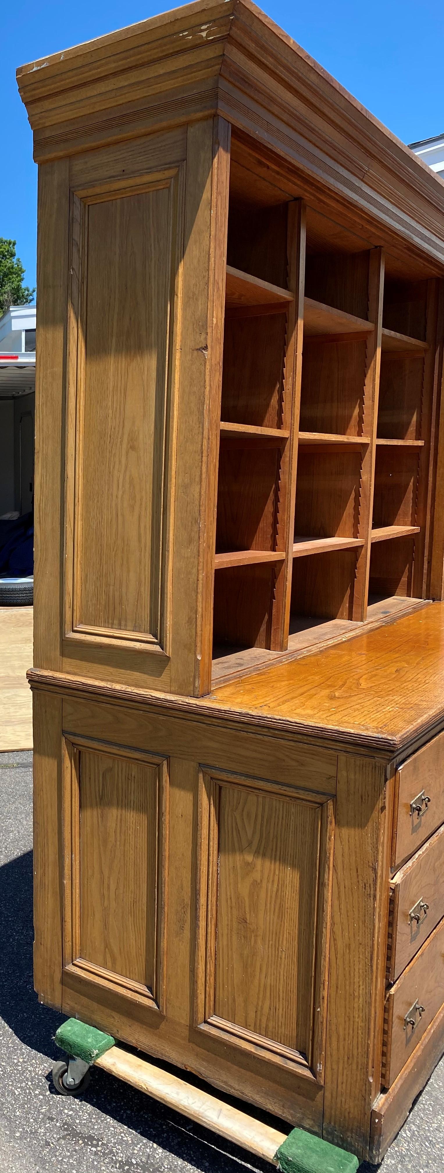 A great large two-piece country store cabinet with upper bookcase with nine adjustable shelves (with two additional in separate photo), over a lower case with nine dovetailed drawers. The piece retains its original brass pulls, but the upper case is