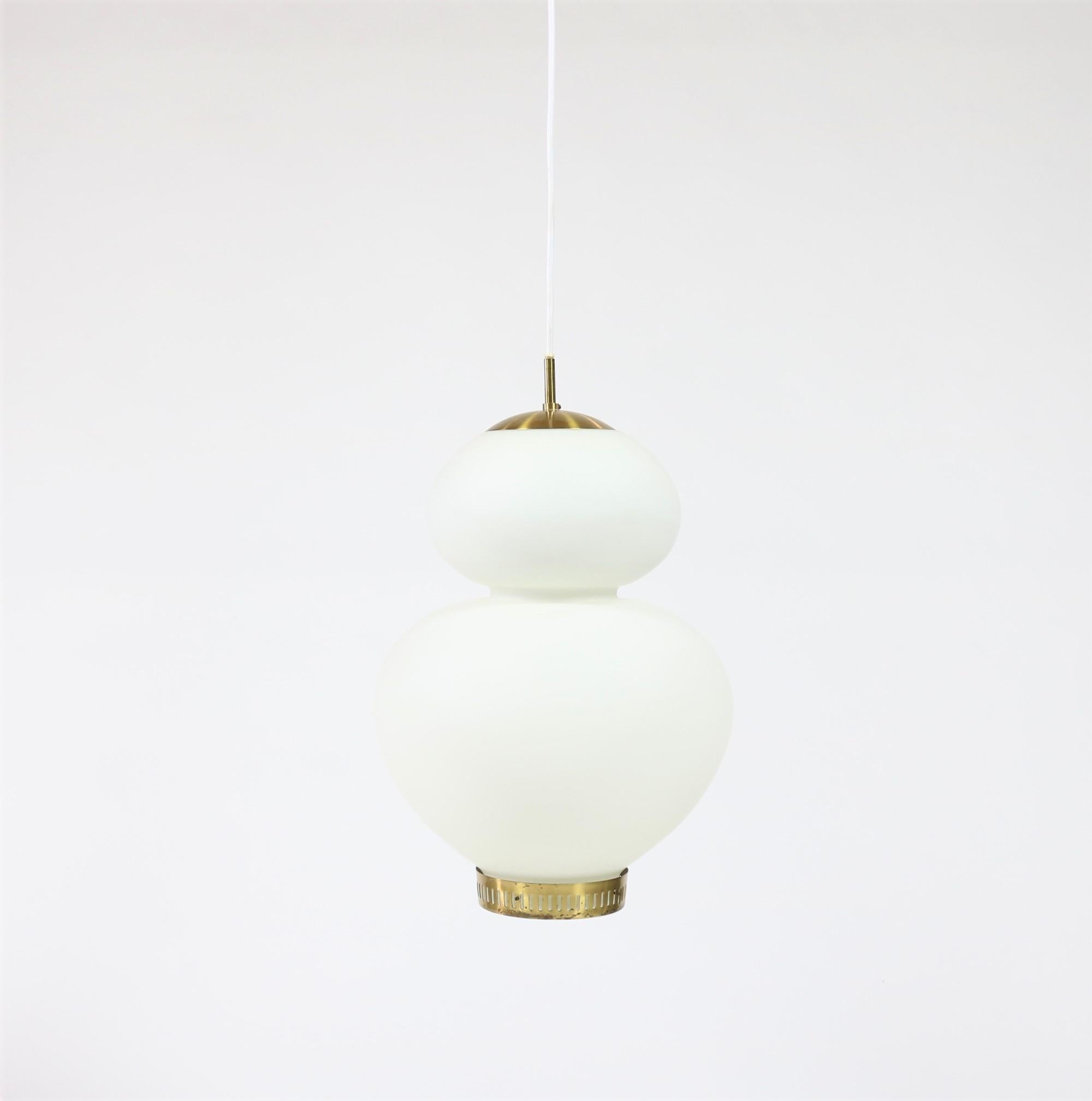 Beautiful pendant from the late 1940s by Danish designer Bent Karlby. Hand-blown opalized glass with an attractive curvy shape, complimented by a brass top and bottom. The brass bottom carries narrow peepholes, a Karlby trademark, and hold an opal