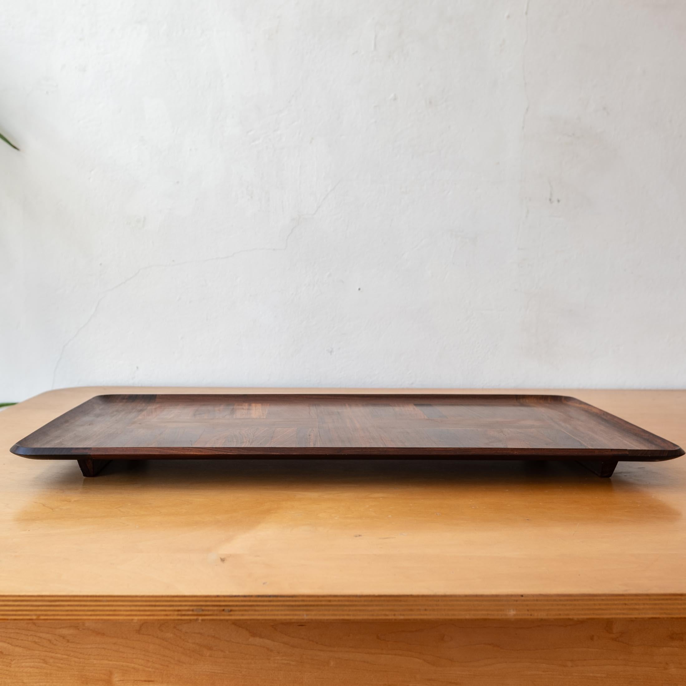 Enorme bandeja diseñada por Jens Quistgaard para la colección Dansk Rare Woods. Es un diseño elegante con esquinas redondeadas esculpidas y patas de trineo para levantar la bandeja de la mesa. Construido en Cocobolo. Presentada en 1961, la línea