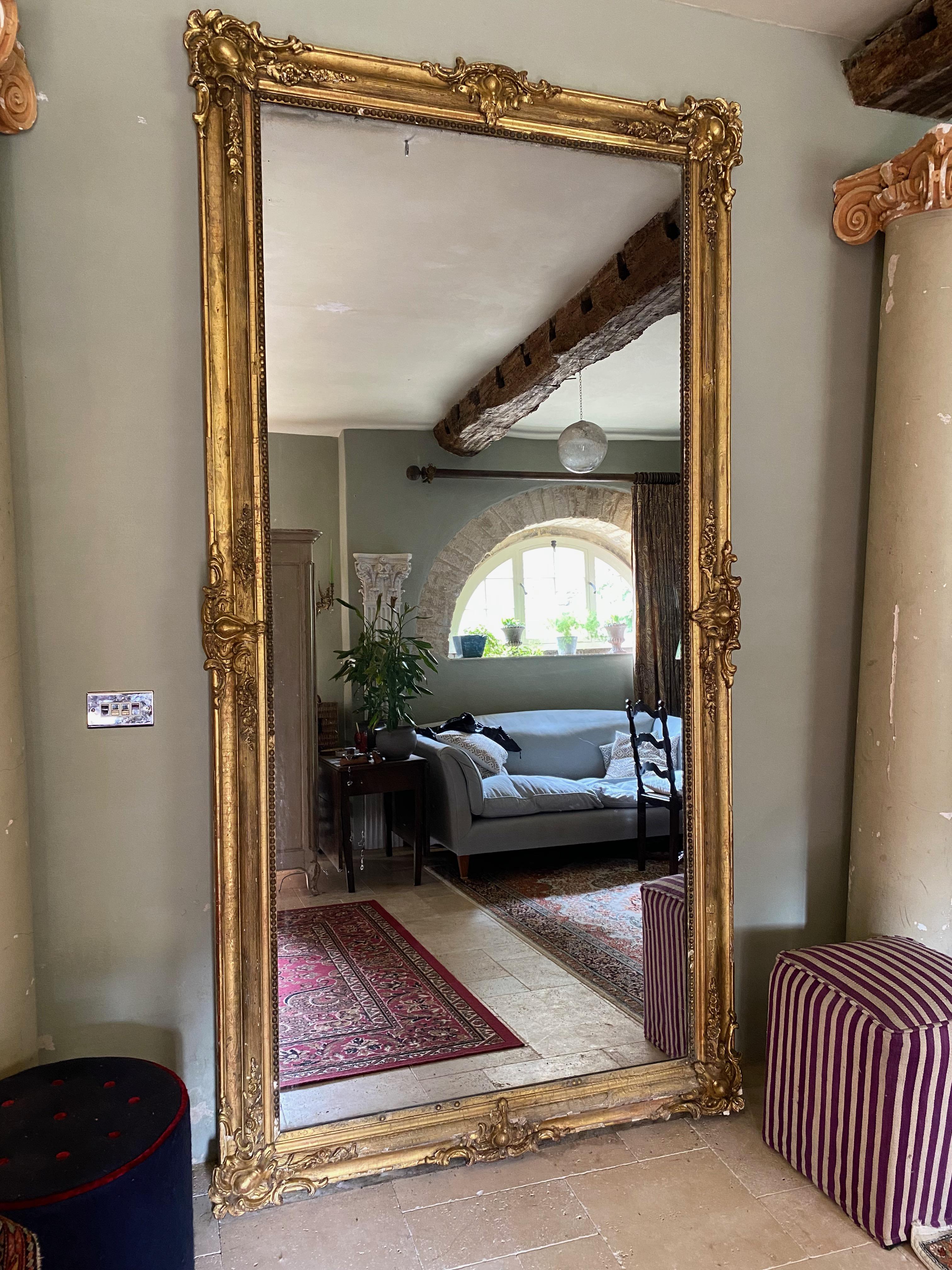 A stunning French gilt wood mirror. Enormous in scale with what appears to be the original glass. The frame is good, but has suffered from loss to the gesso. The lower piece of the frame (when standing portrait) has lost its gilding - possibly
