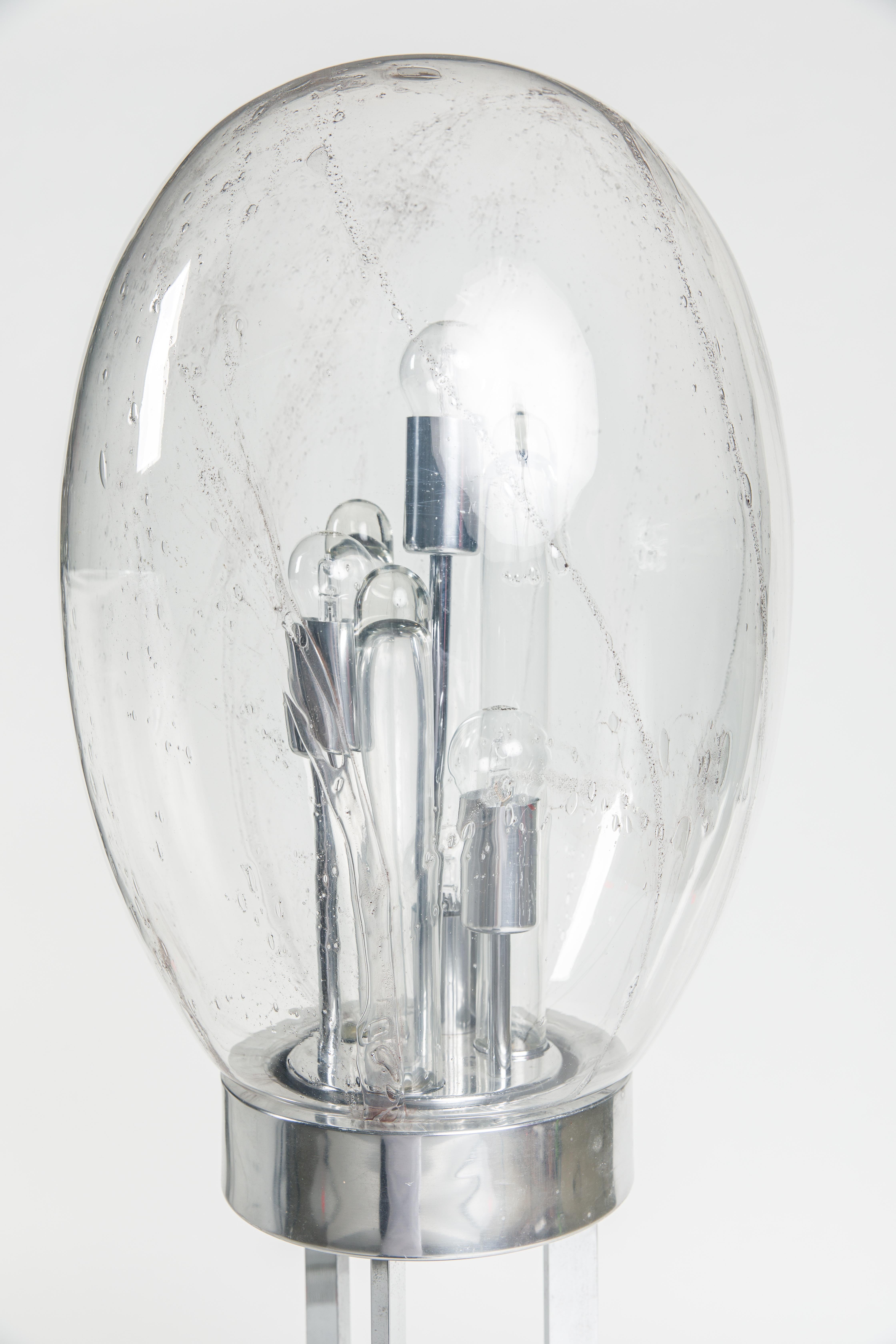 Lampadaire des années 1960-1970, fabriqué par Doria en Allemagne.
Socle en métal chromé, diffuseur sphérique ovale en verre clair avec inclusions de baudruche, quatre brûleurs et trois tubes en verre à l'intérieur. Labellisé sur la face