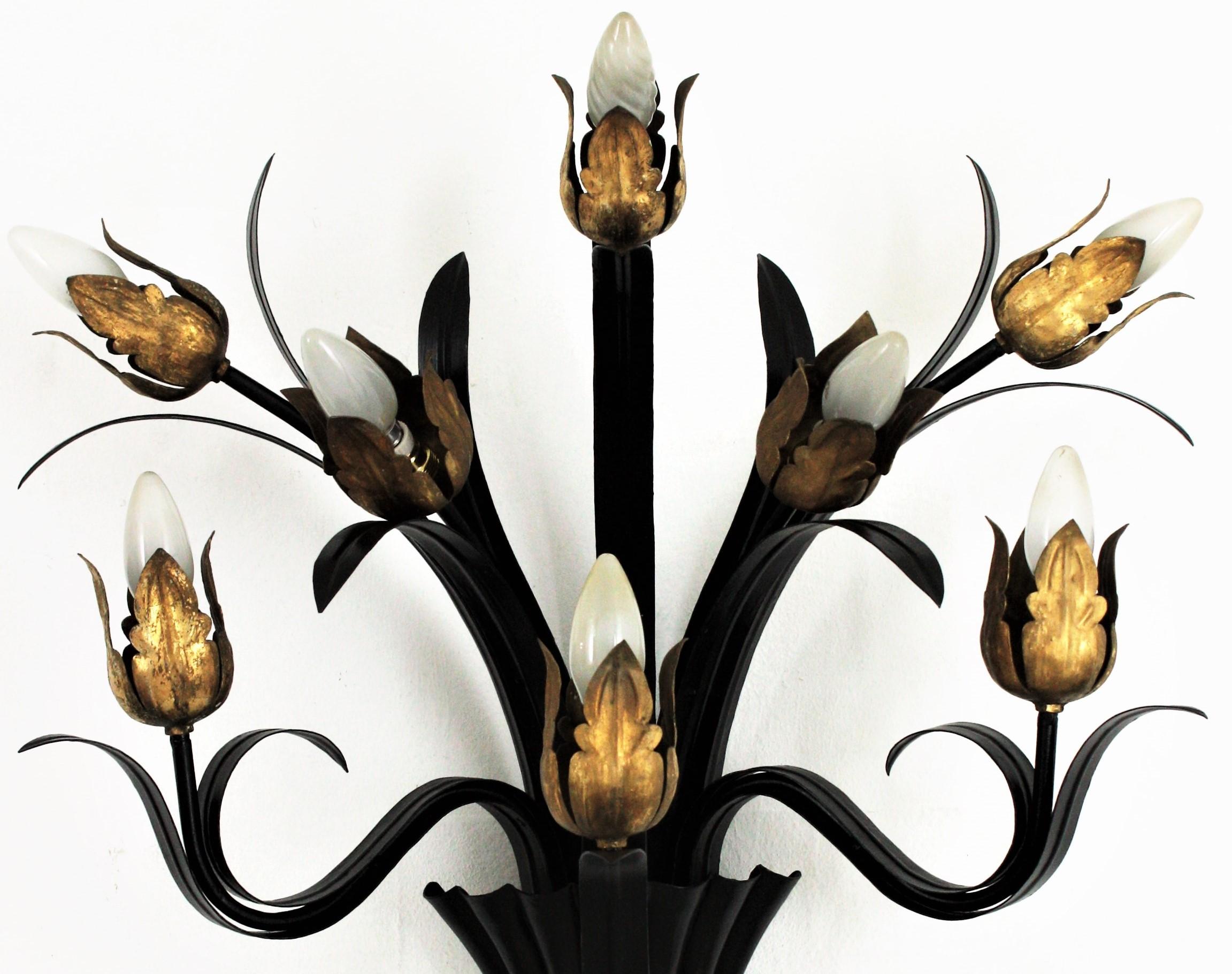 Eye-catching gilt and black iron eight-light flower buds wall sconce. Spain, 1950s.
This large wall sconce is heavily and beautifully constructed. It has 8 leafed arms with flower bud endings hiding the bulb holders.
The finishing combining a