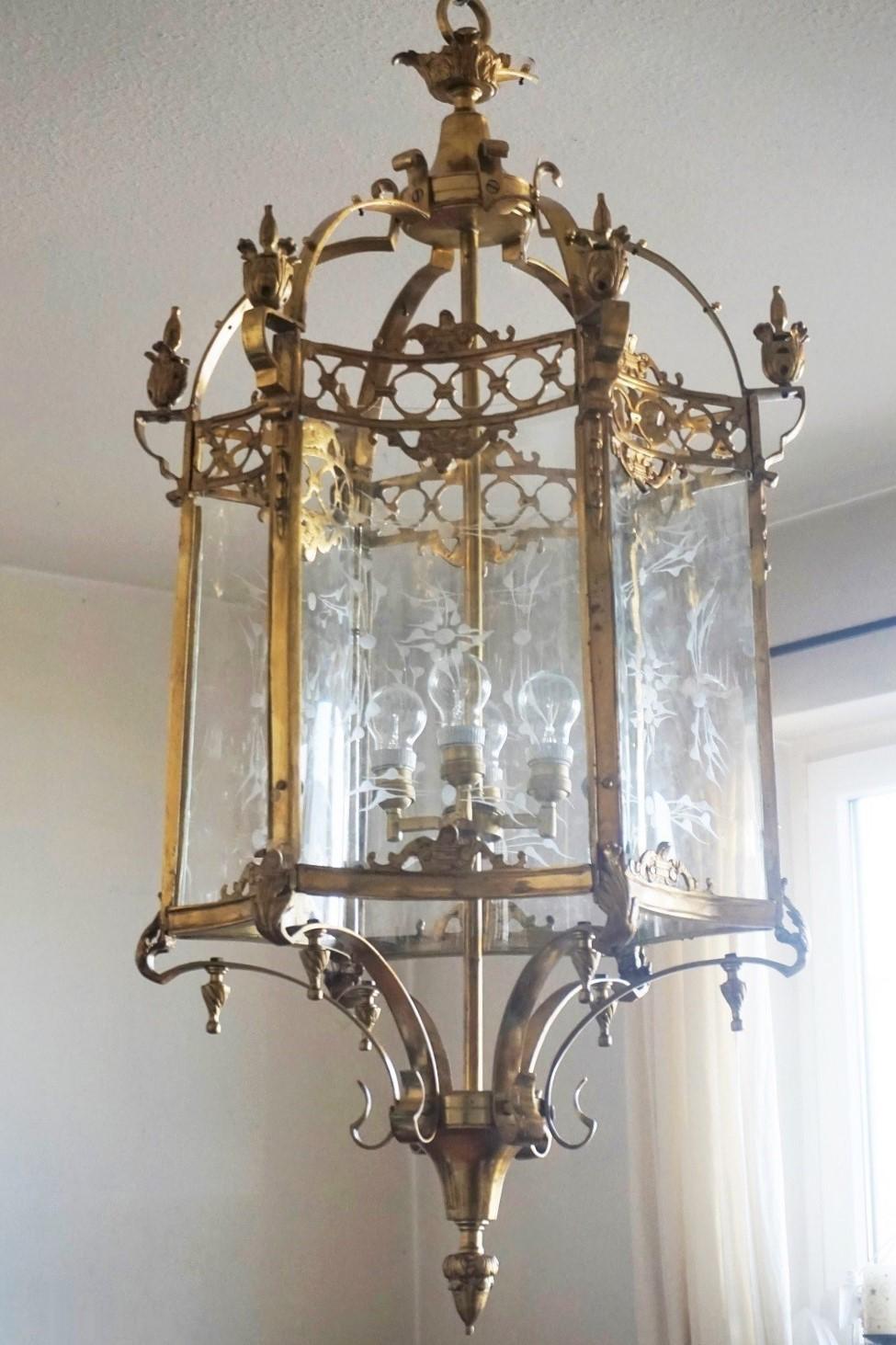 Très grande lanterne hexagonale à quatre lumières de style Louis XVI, France, 1920-1930. La lanterne est fabriquée en laiton massif avec des détails en bronze moulé intégrés, six côtés incurvés avec des panneaux en verre découpé incurvés. Chaîne et