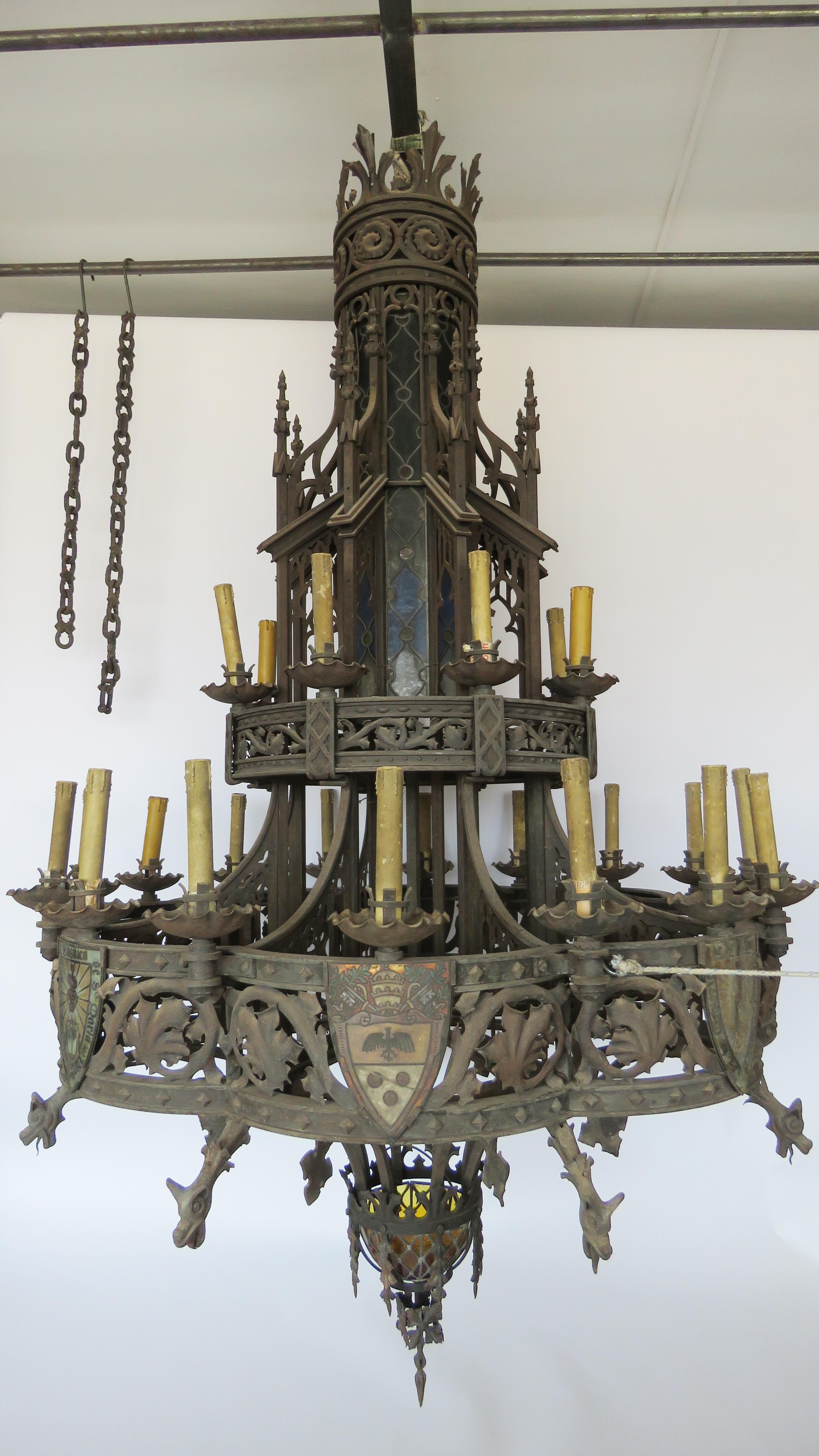 Huge hammered iron chandelier of great Gothic influence with painted Cristal coat of arms set on intricate detailed ironwork with scrolls, foliage, dragons and stained glass windows. Provenance: Basilica Santa Maria del Pino.