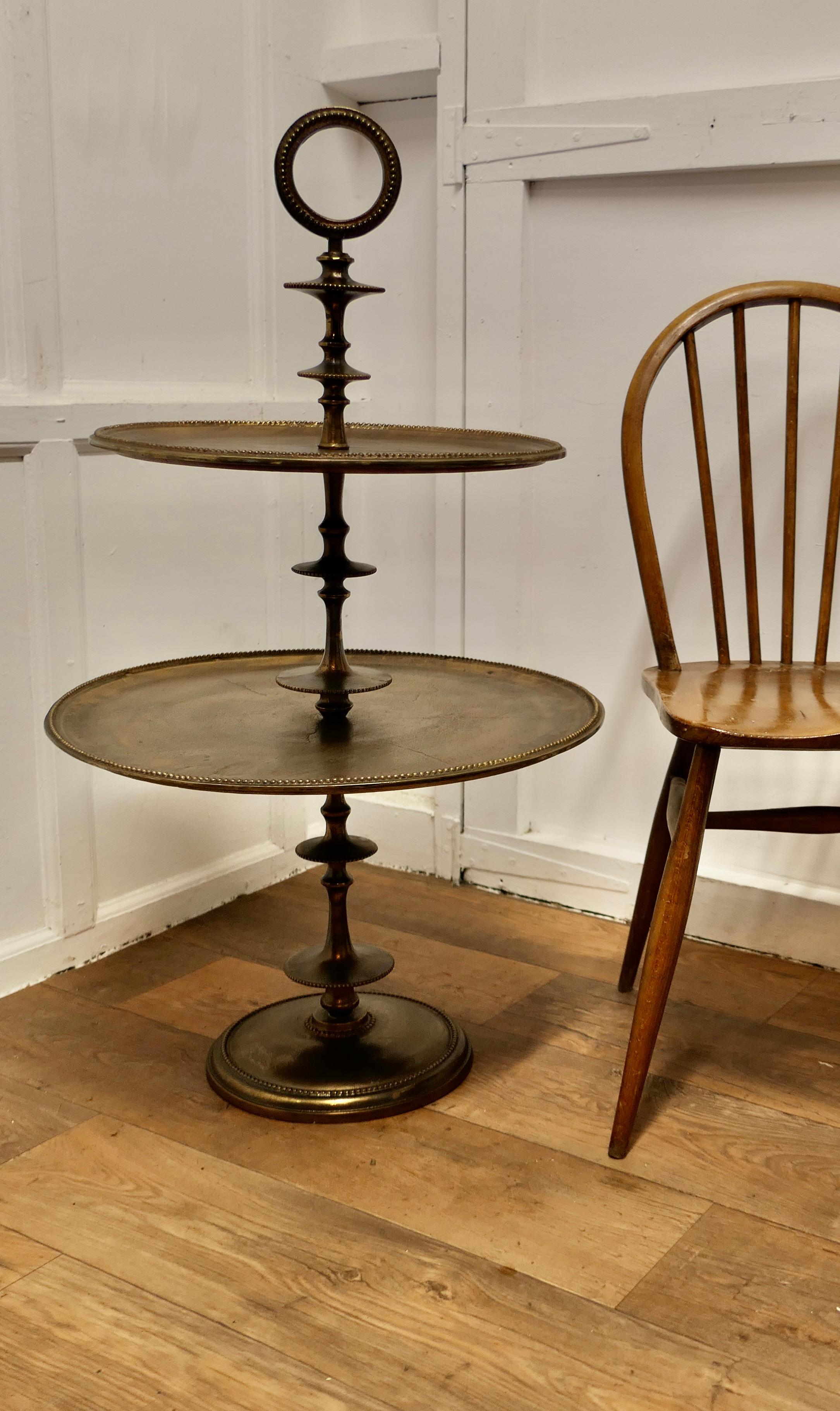 Huge Gueridon Cake Stand or Dumb Waiter 

A charming and unusual piece in good condition, it has 2 tiers,  it is made in iron which has a charming bronzed patina, it has a turned central column and a large ring handle at the very top
The stand is in