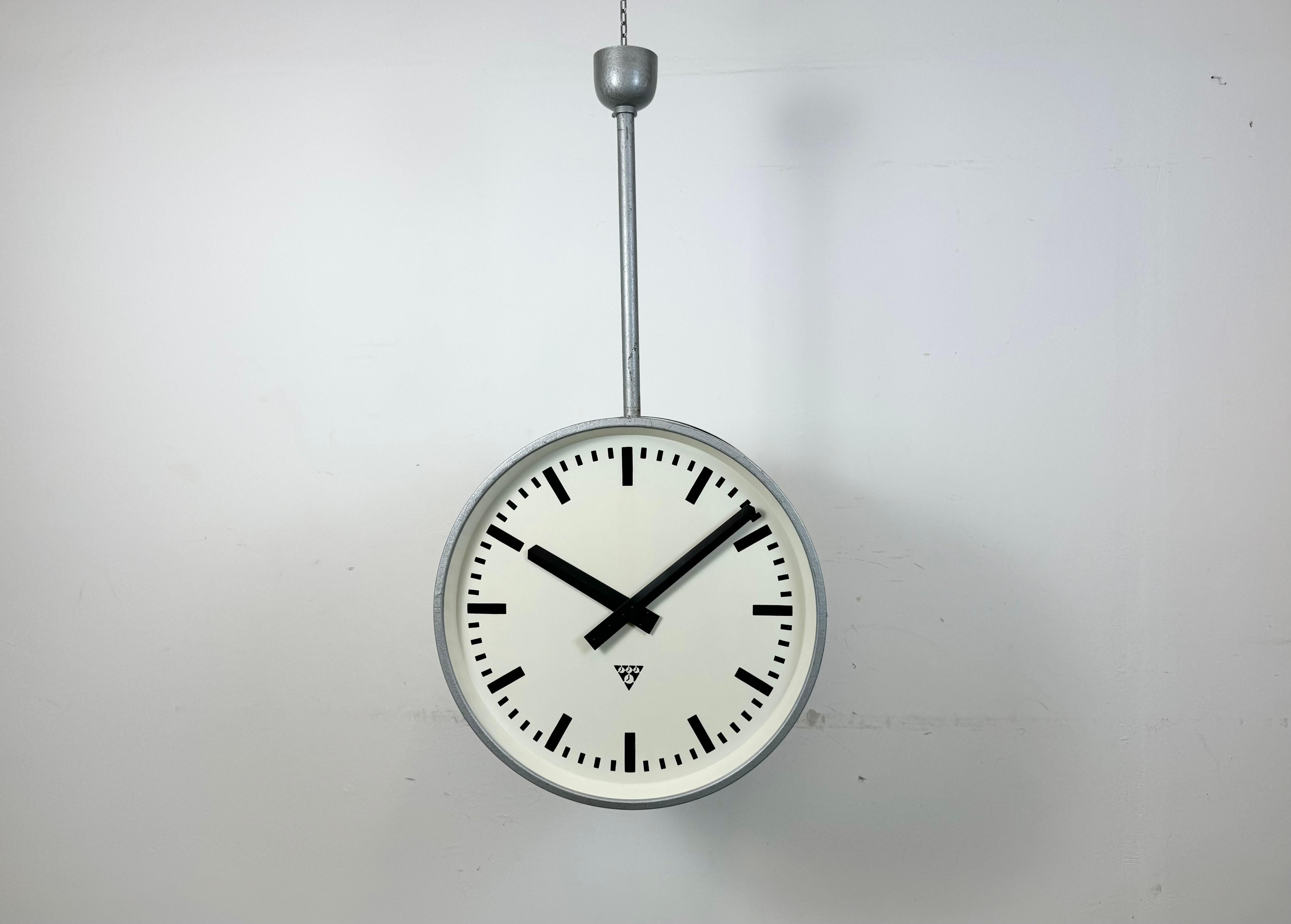 This large double sided railway or factory clock was produced by Pragotron, in former Czechoslovakia, during the 1960s. The piece features a grey metal body and a clear glass cover. The clock has been converted into a battery-powered clockworks and