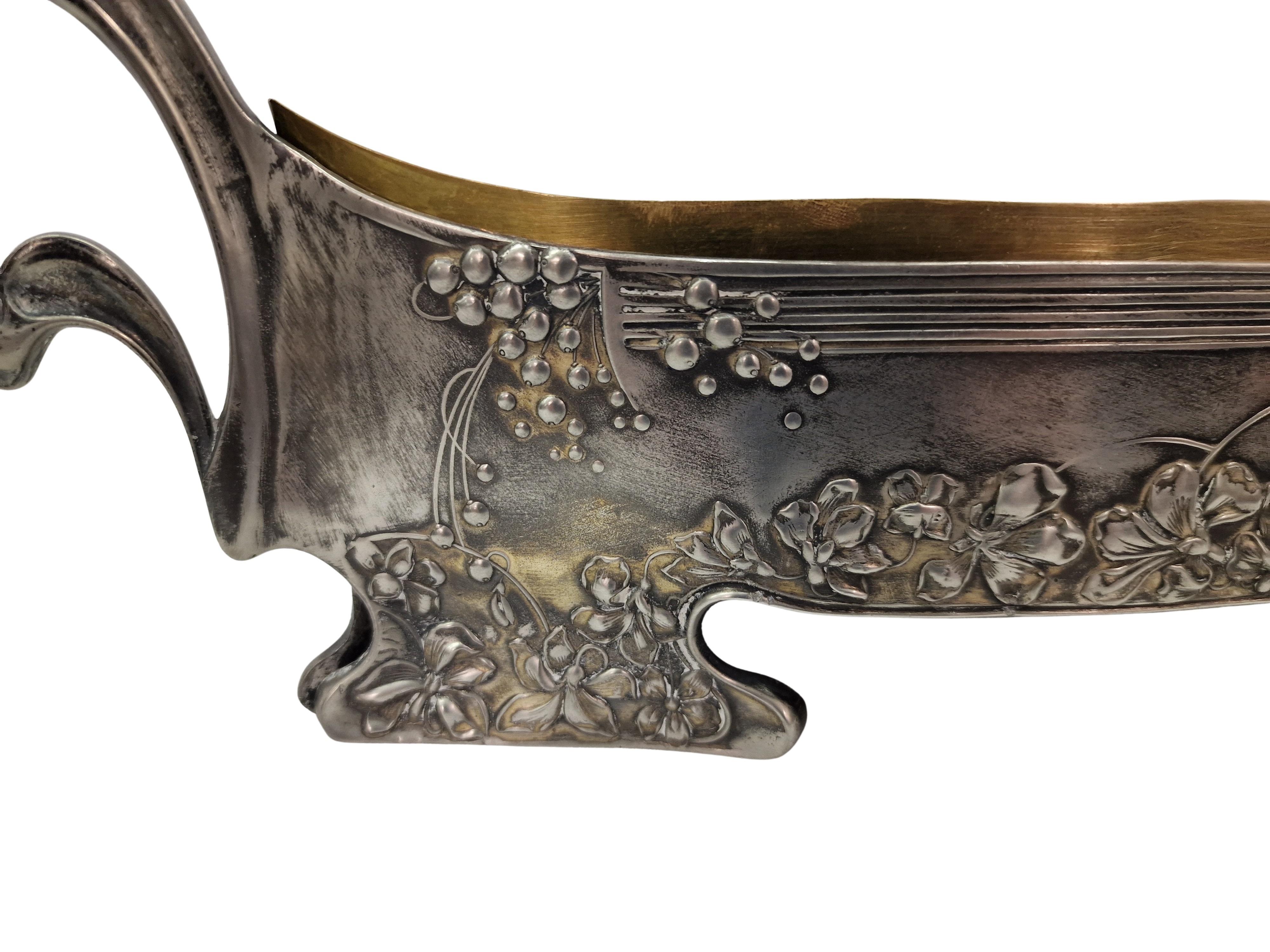 Jardiniere purement Jugendstil, fabriquée au début du siècle 1900, en Autriche par le célèbre orfèvre Moritz Hacker. 

L'objet est composé de deux pièces. L'extérieur est en métal argenté et l'intérieur en laiton massif. La jardinière est décorée