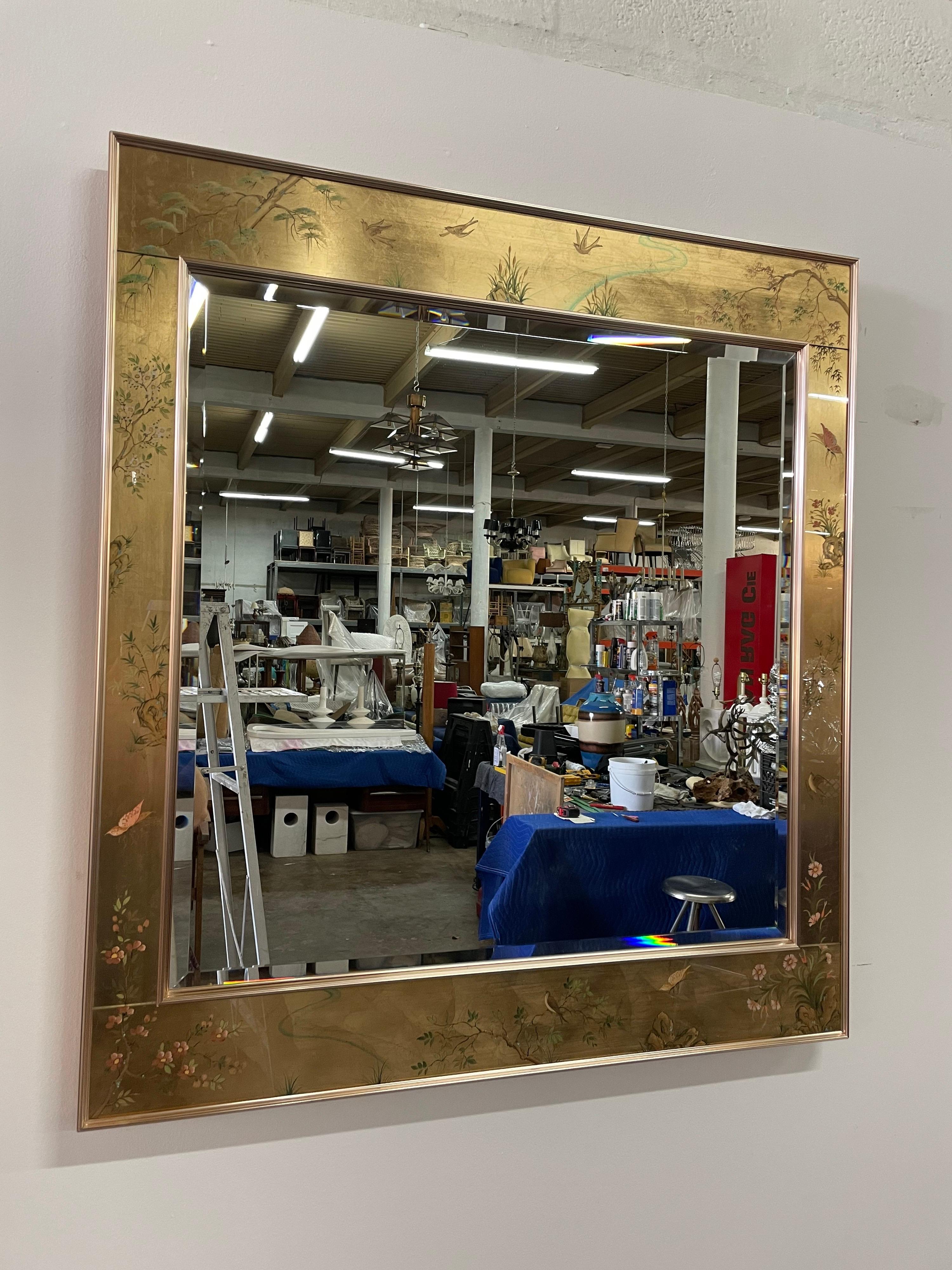 Ce magnifique et élégant miroir biseauté peint à la main en chinoiserie inversée et encadré de feuilles d'or, Signé en bas (K, Widing). Le cadre en aluminium doré entoure le miroir biseauté et la bande décorative. C'est le plus grand de ce modèle