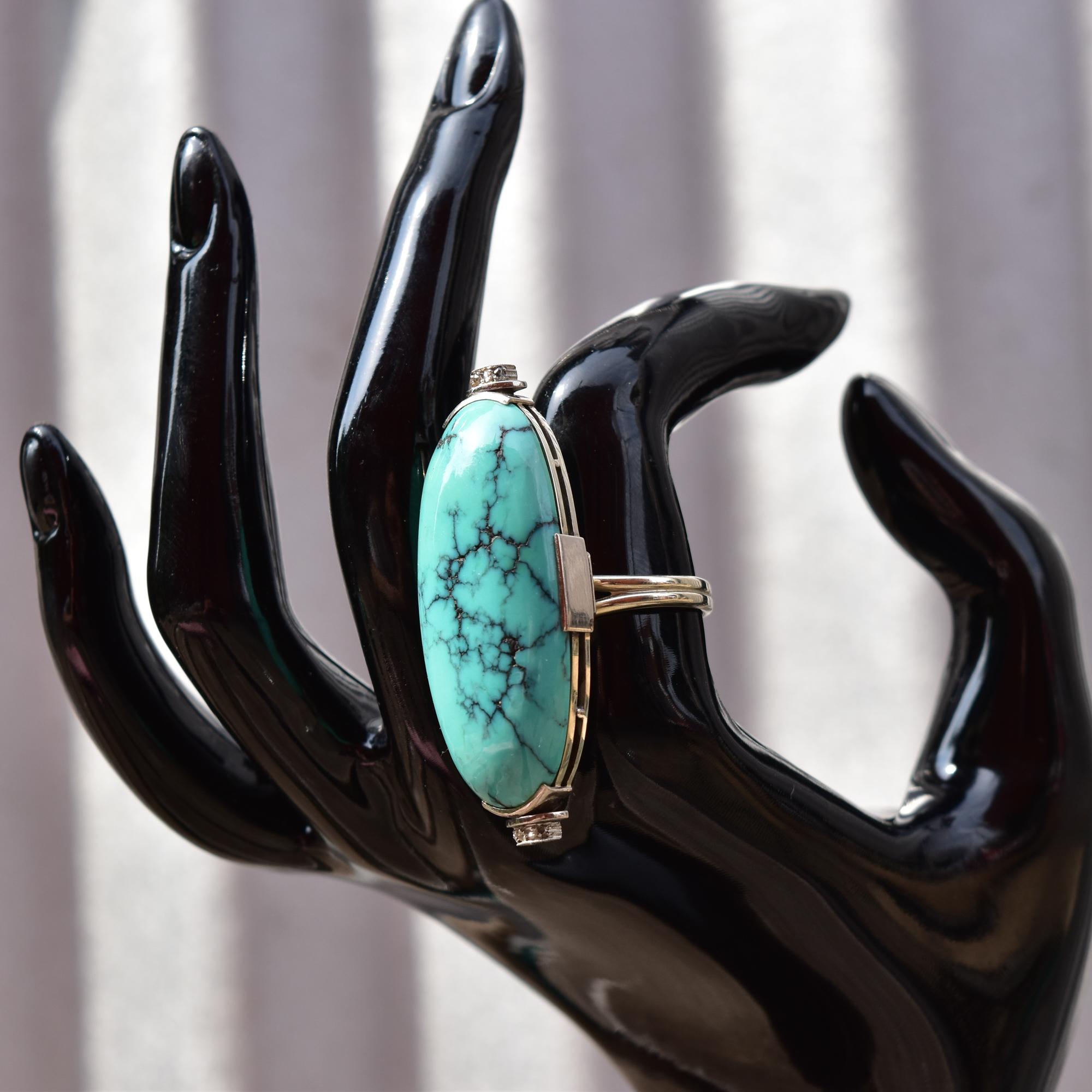 A huge turquoise cabochon diamond accent statement ring set in platinum and 14k white gold. Features a long-cut turquoise cabochon mounted in a platinum bezel setting with 4-diamond chip embellishments on each end. The turquoise has a bright blue