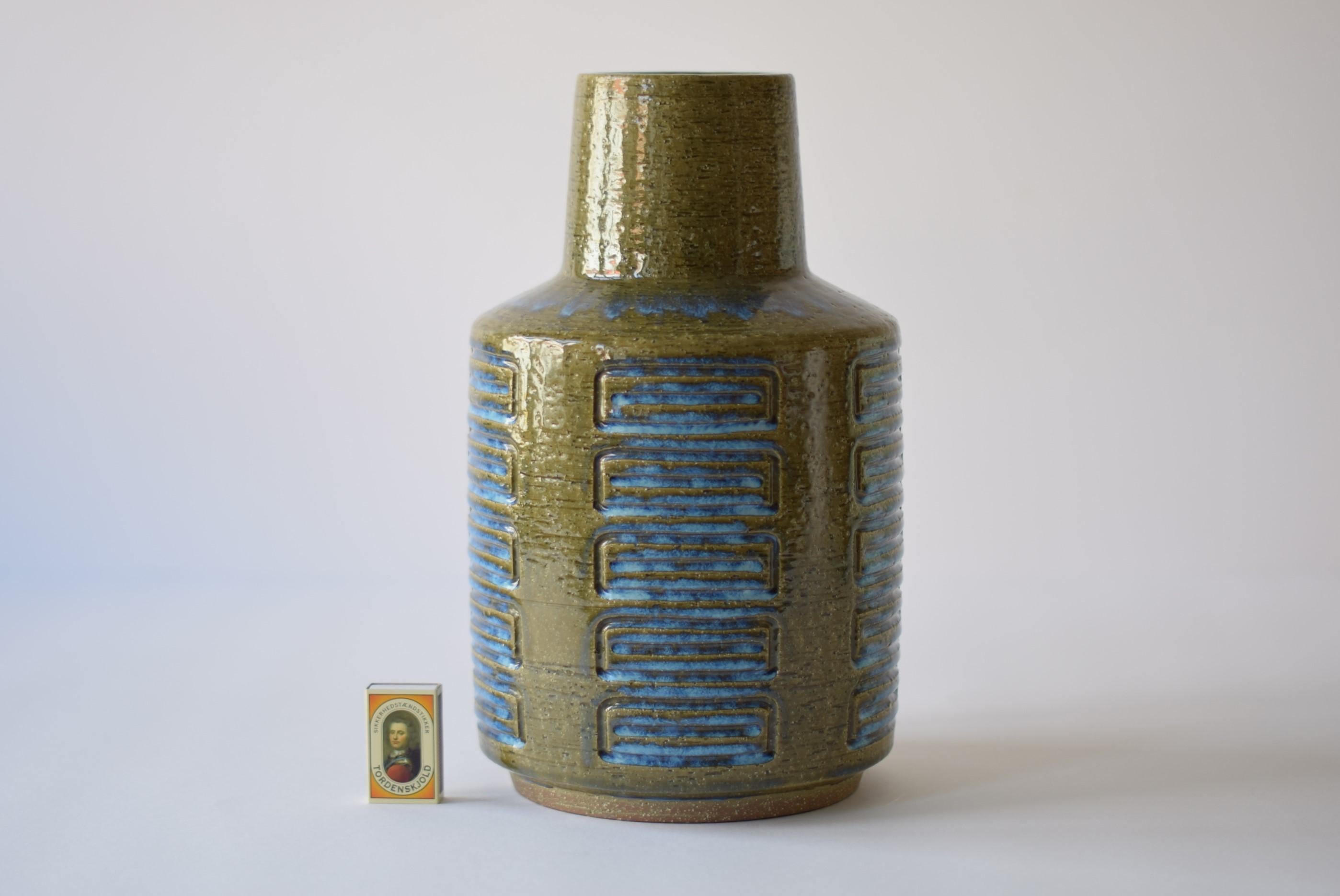 This huge budded vase was designed by Per Linnemann-Schmidt for Palshus and was produced in Denmark during the 1960s or early 1970s. It has a shiny glaze in moss green with blue in the incised stripes and on the shoulder. The vase is made with the