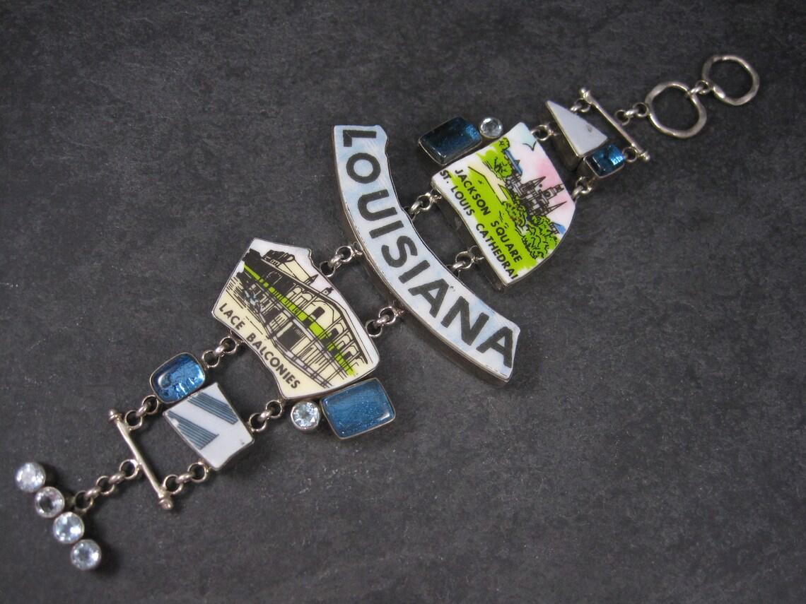 This huge, gorgeous designer, sterling bracelet features pieces from a hand painted 1950s era commemorative plate, fused glass and natural blue topaz gemstones.
It is the creation of Aurora Glass Jewelry artist Patti Quinn.

This bracelet measures 2