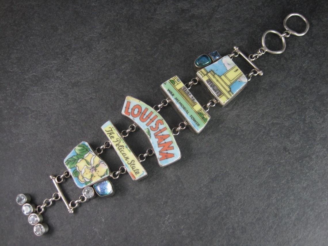 This huge, gorgeous designer, sterling bracelet features pieces from a hand painted 1950s era commemorative plate, fused glass and natural blue topaz gemstones.
It is the creation of Aurora Glass Jewelry artist Patti Quinn.

This bracelet measures 1