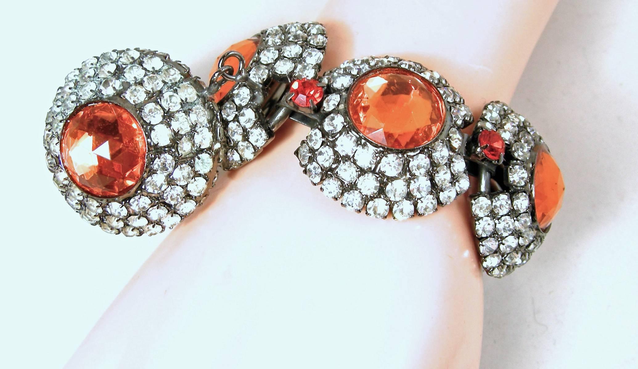 This is a magnificent Larry Vrba’s early 1970s bracelet with 5 huge links with rows of crystals leading up to an orange stone center. In-between each link is an orange crystal.  It has a fold-over clasp in a pewter metal finish.  At the end, there