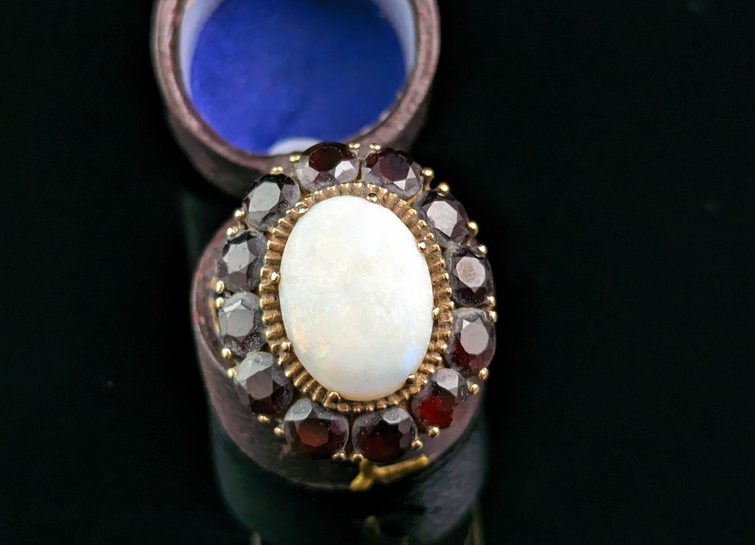 Ein großer Vintage Opal und Granat Cluster Ring in 9ct Gold.

Dieser Clusterring in Übergröße ist ein echtes Schmuckstück, das auf jeden Fall auffallen soll.

Er ist aus 9-karätigem Gelbgold gefertigt, mit einem glatten, polierten Band und hübschen,