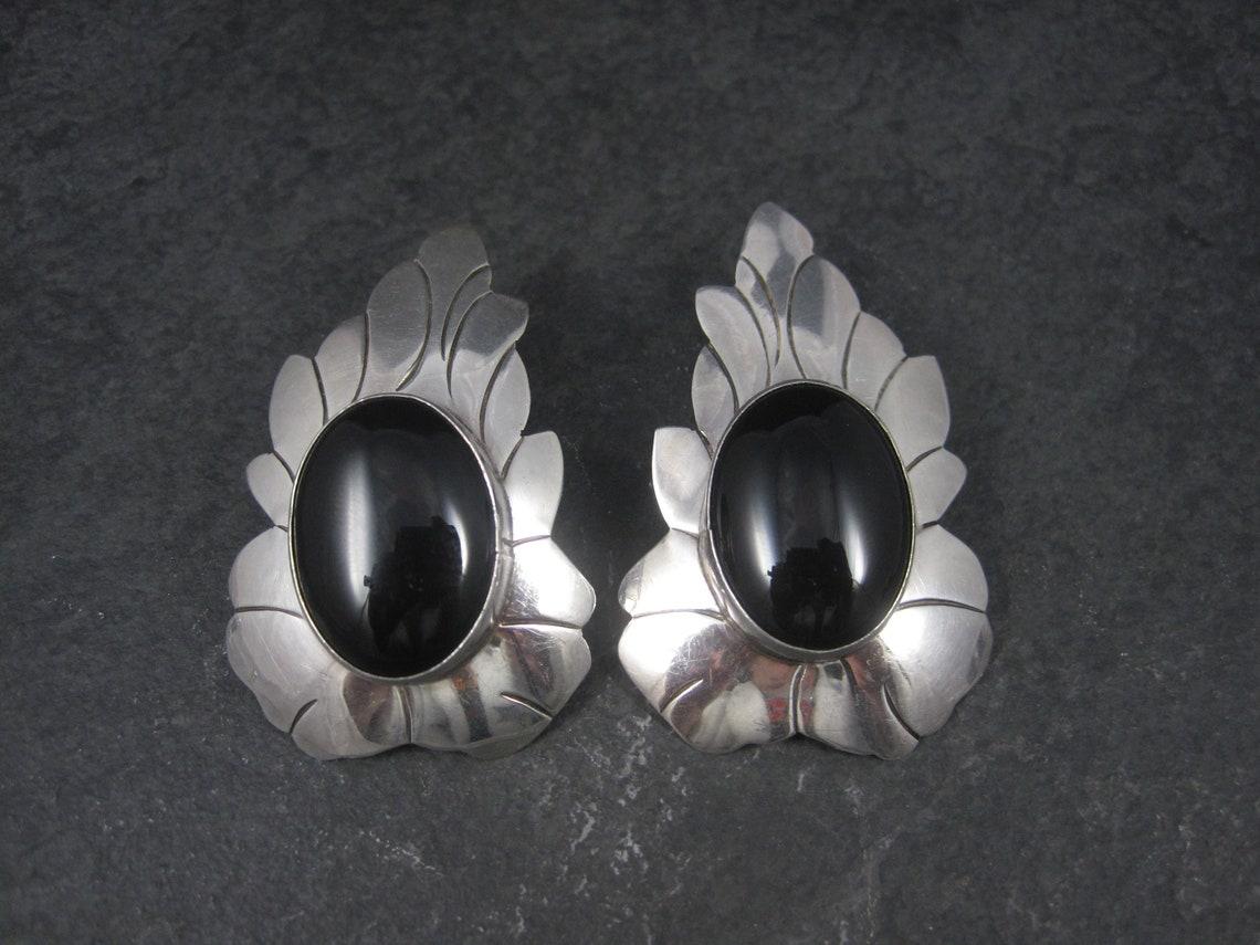 These huge, gorgeous Southwestern earrings are sterling silver with 17x24mm onyx stones.

Measurements: 1 3/8 by 2 1/4 inches
Weight: 22.2 grams

Marks: Sterling, JA
I believe this hallmark belongs to Navajo silversmith Juan Alberta

Condition: